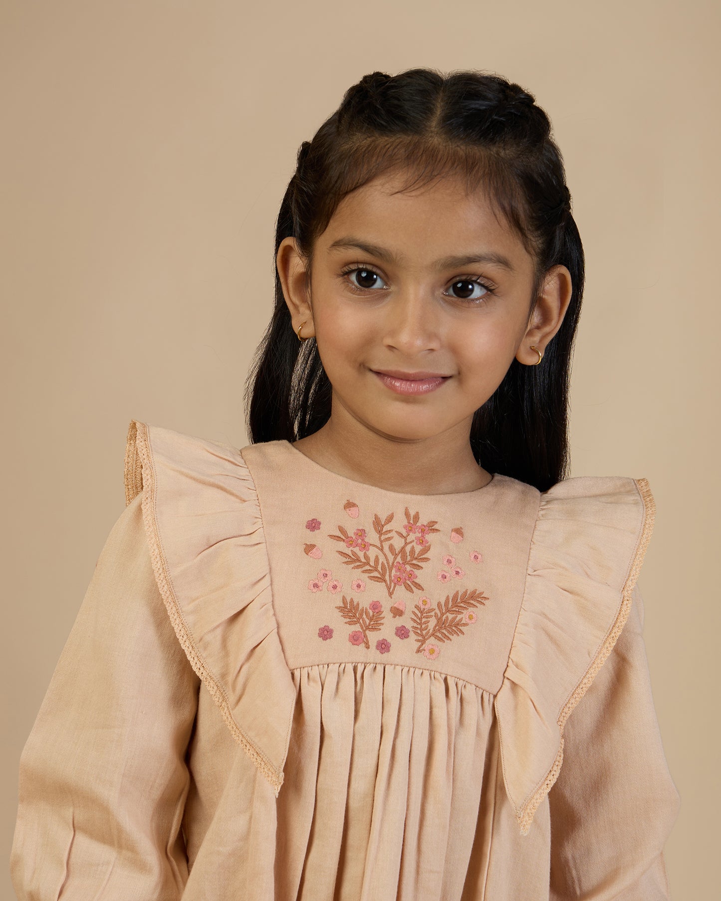 Early Sunday, Margot Dress in Beige, made from Cotton Satin fabric, featuring classic silhouette with floral embroidery around the yoke and ruffle detailing, shown in a front view of a model wearing it in a studio setting