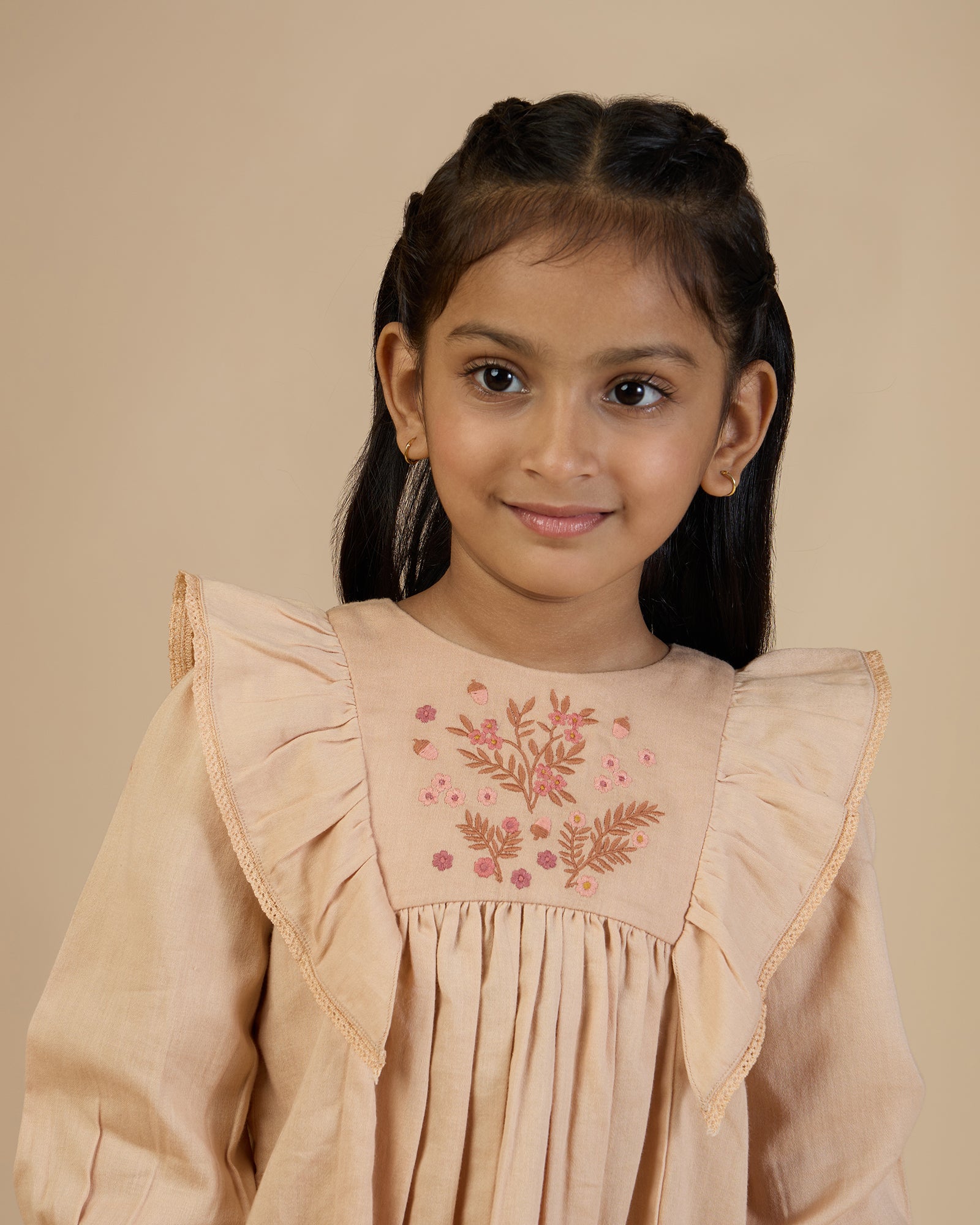 Early Sunday, Margot Dress in Beige, made from Cotton Satin fabric, featuring classic silhouette with floral embroidery around the yoke and ruffle detailing, shown in a front view of a model wearing it in a studio setting
