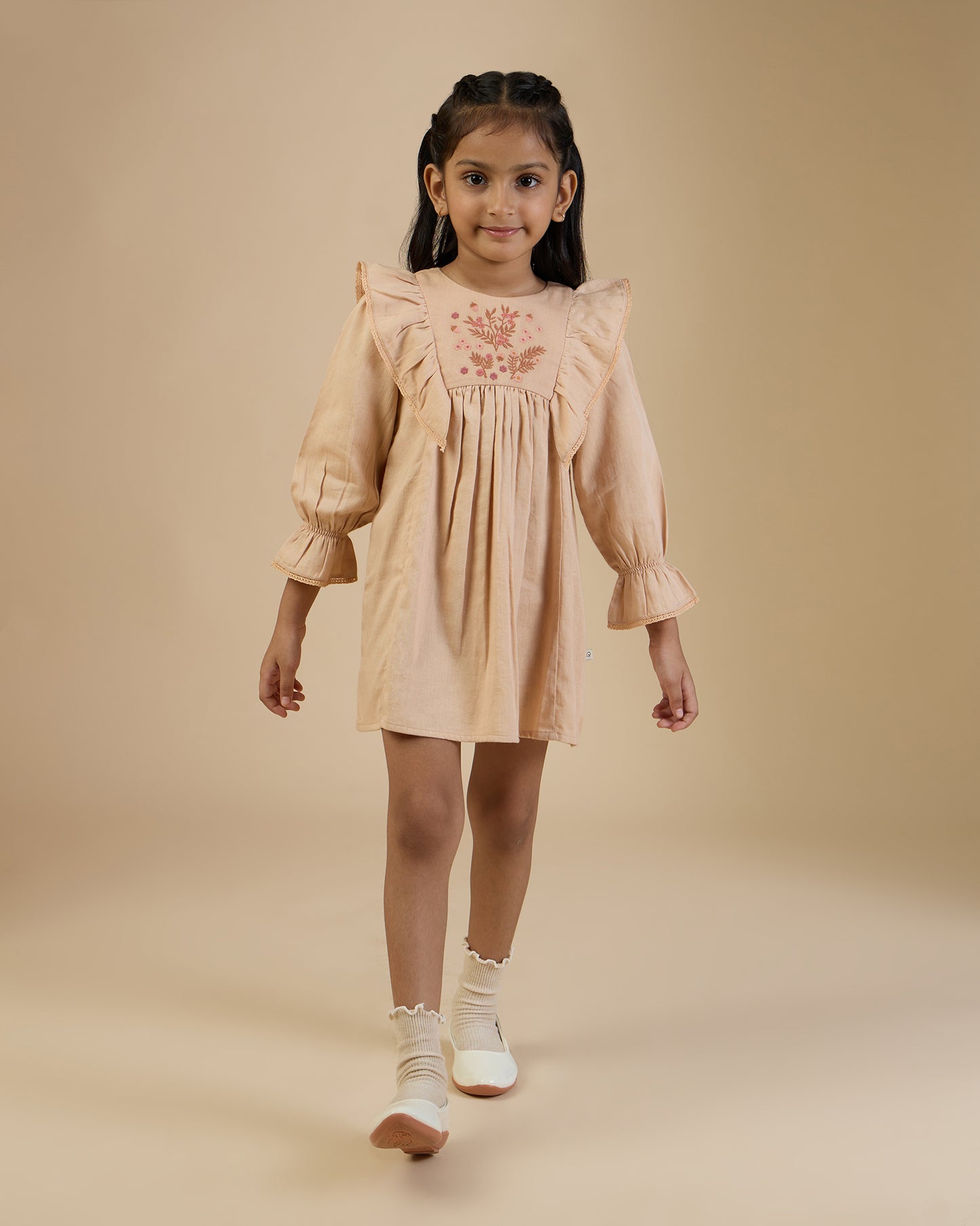 Early Sunday, Margot Dress in Beige, made from Cotton Satin fabric, featuring classic silhouette with floral embroidery around the yoke and ruffle detailing, shown in a front view of model wearing it