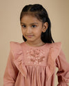 Early Sunday, Margot Dress in Earthy Pink, made from Cotton Satin fabric, featuring classic silhouette with floral embroidery around the yoke and ruffle detailing, shown in a front view of a model wearing it in a studio setting