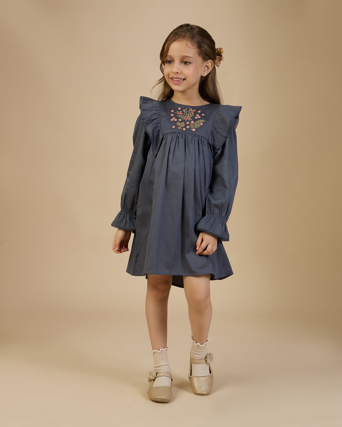 Early Sunday, Margot Dress in Stormy Blue, made from Cotton Satin fabric, featuring classic silhouette with floral embroidery around the yoke and ruffle detailing, shown in a front view of model wearing it