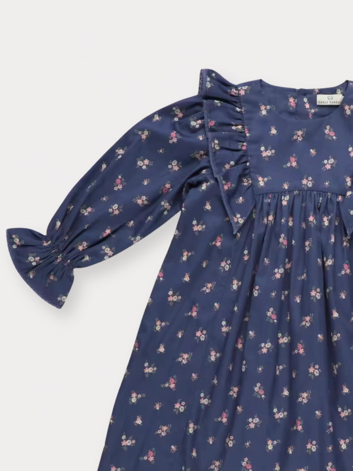 Early Sunday, Margot Dress in Ditsy Bouquet Navy, made from Printed Cotton Satin fabric, featuring classic silhouette with ruffle detailing around the sleeves, shown in a closeup flat-lay view