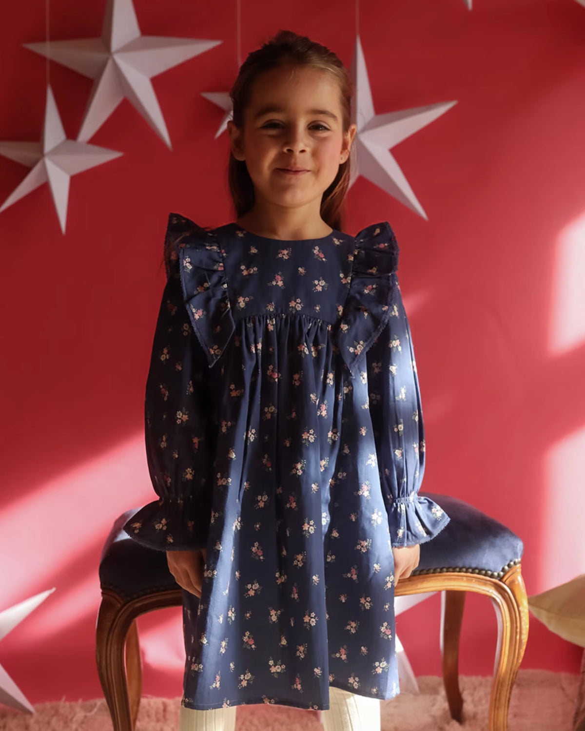 Early Sunday, Margot Dress in Ditsy Bouquet Navy, made from Printed Cotton Satin fabric, featuring classic silhouette with ruffle detailing around the sleeves, shown in a front view of model wearing it