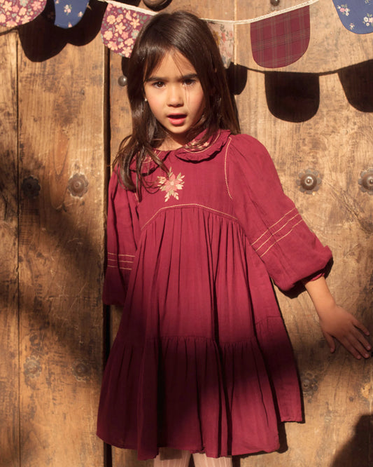 Early Sunday, Marguerite Dress in Plum, made from Cotton Double Gauze fabric, featuring floral embroidery with frilled Peter Pan collar, shown in a front view of model wearing outdoors