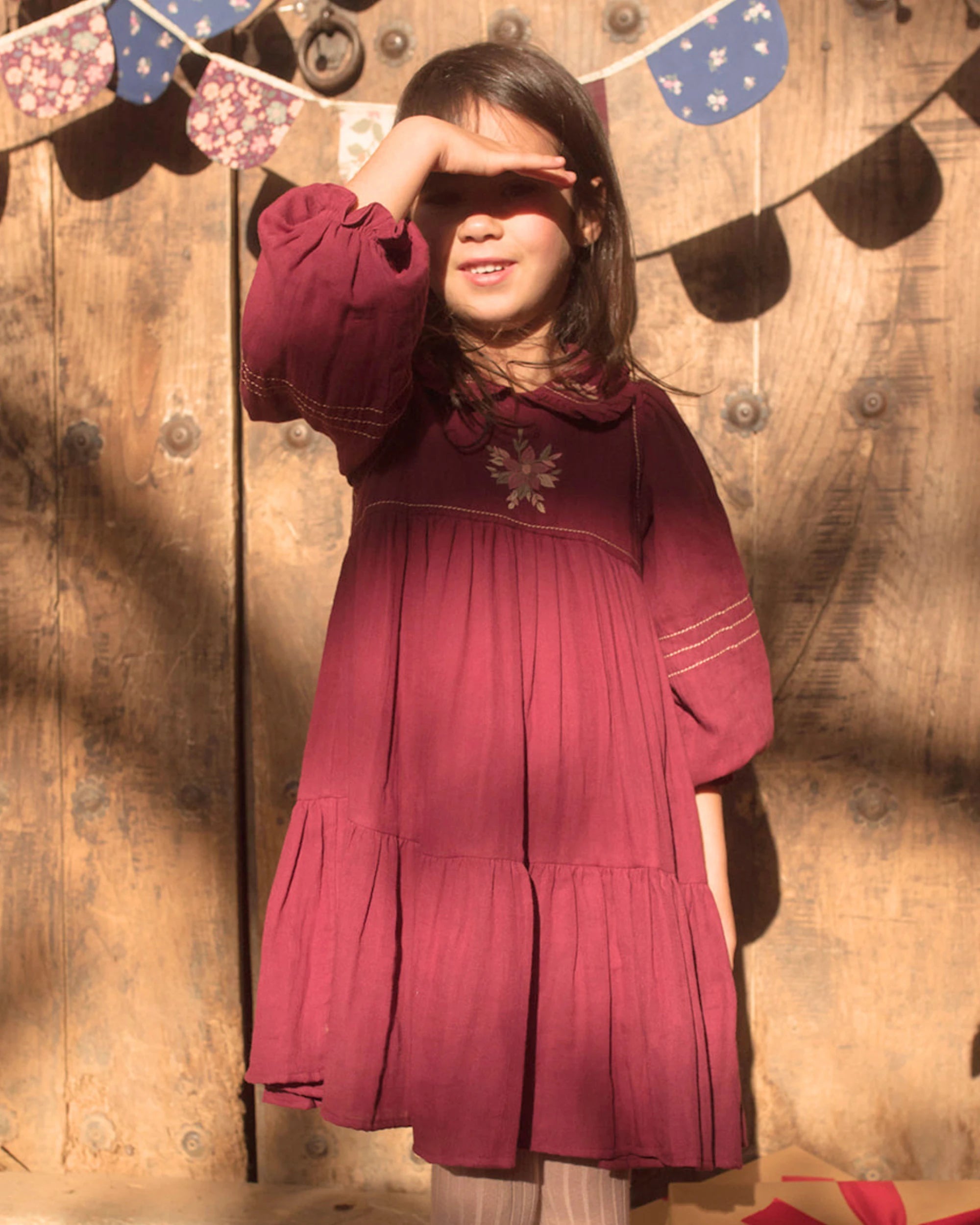 Early Sunday, Marguerite Dress in Plum, made from Cotton Double Gauze fabric, featuring floral embroidery with frilled Peter Pan collar, shown in a front view of model playing outdoors