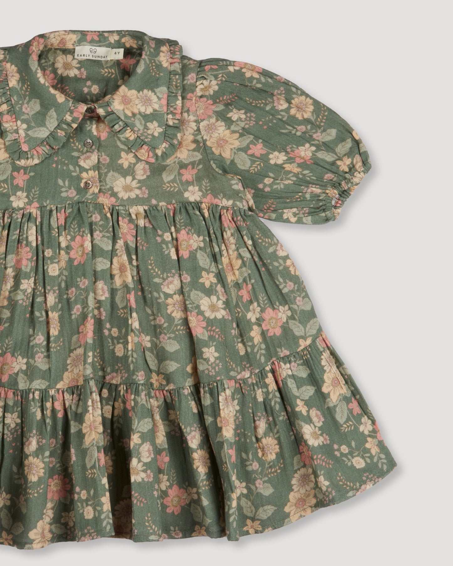 Early Sunday, Marguerite Dress in Autumn Bloom Soft Green, made from Printed Cotton Double Gauze fabric, featuring classic silhouette with a collar and ruffle detailing, shown in a closeup flat-lay view