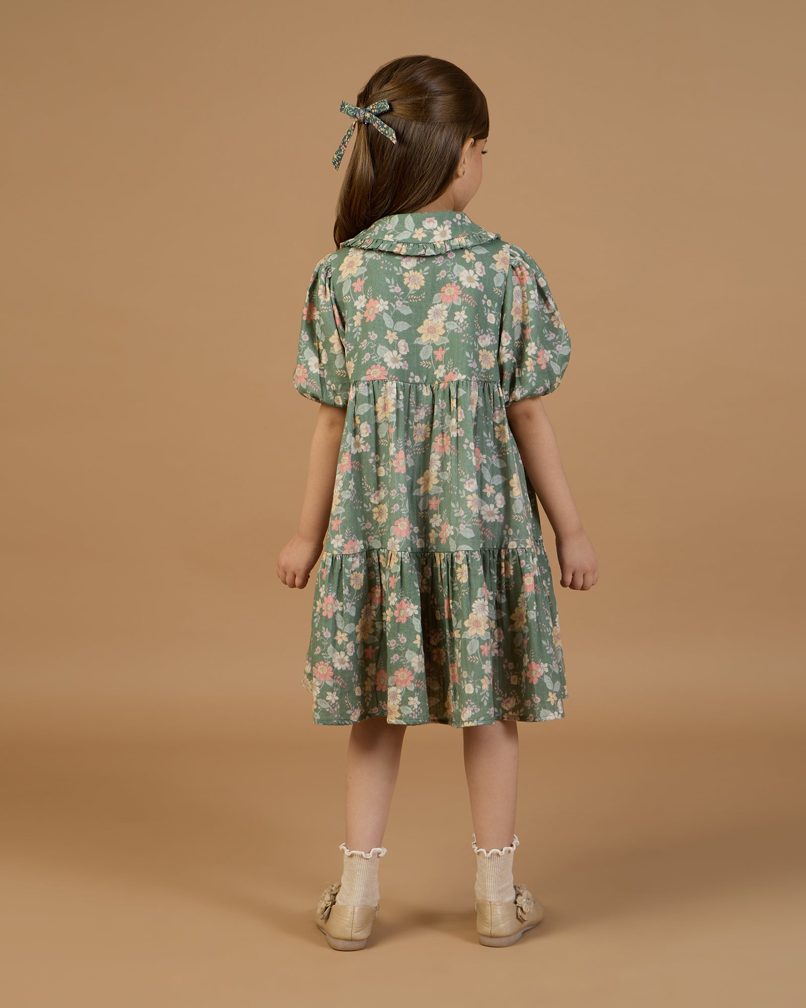 Early Sunday, Marguerite Dress in Autumn Bloom Soft Green, made from Printed Cotton Double Gauze fabric, featuring classic silhouette with a collar and ruffle detailing, shown in a back view of model wearing it