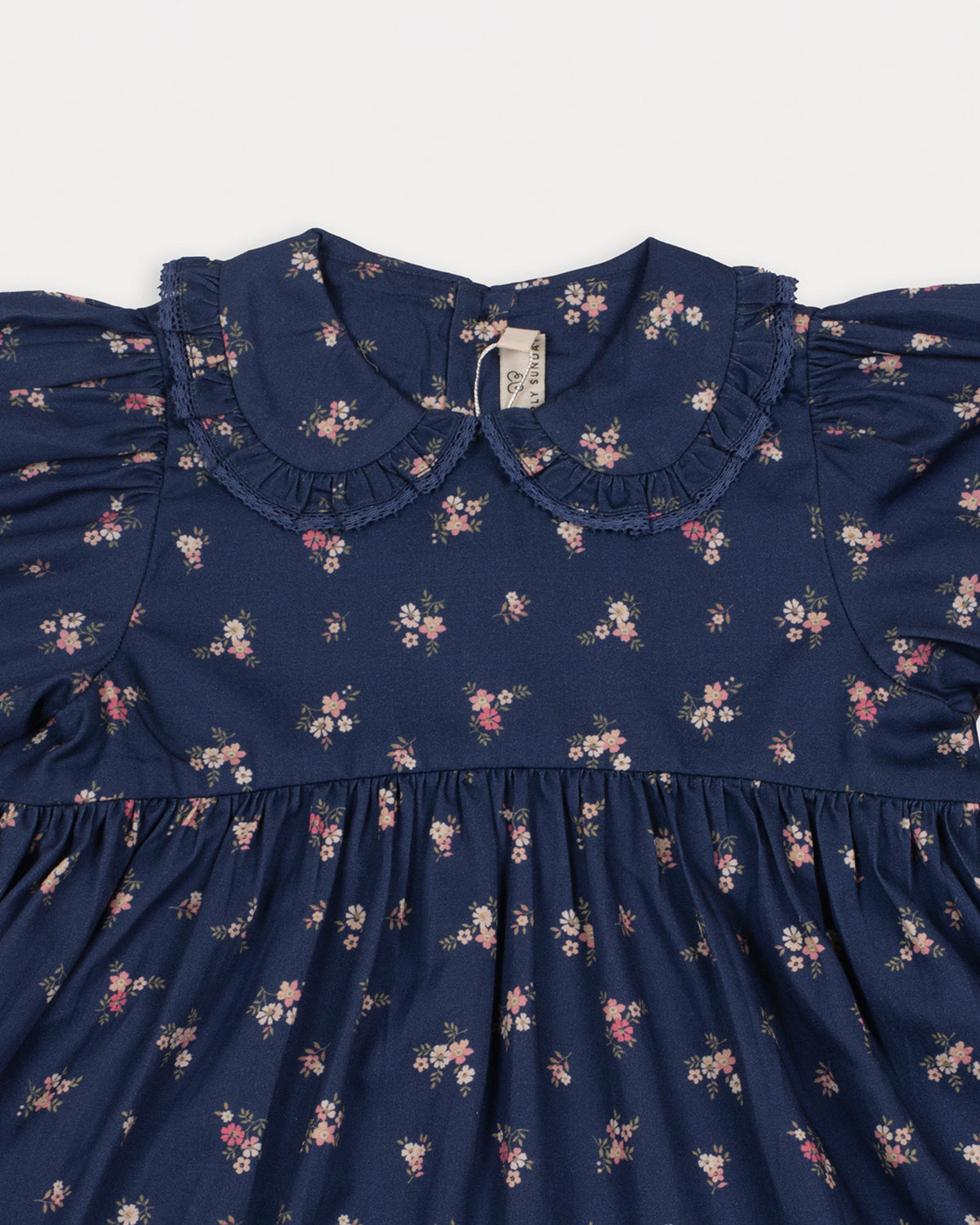Early Sunday, Marguerite Dress in Ditsy Bouquet Navy, made from Printed Cotton Satin fabric, featuring gathered sleeves with frilled Peter Pan collar, shown in a closeup flat-lay view