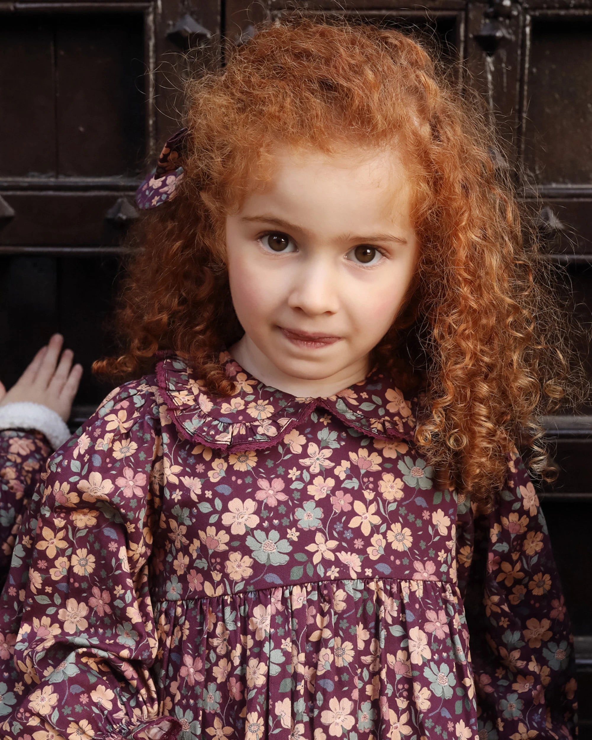 Early Sunday, Marguerite Dress in Garden Flowers Plum, made from Printed Cotton Satin fabric, featuring floral print and detailed lace yoke with Peter Pan collar, shown in a close up shot of model wearing it