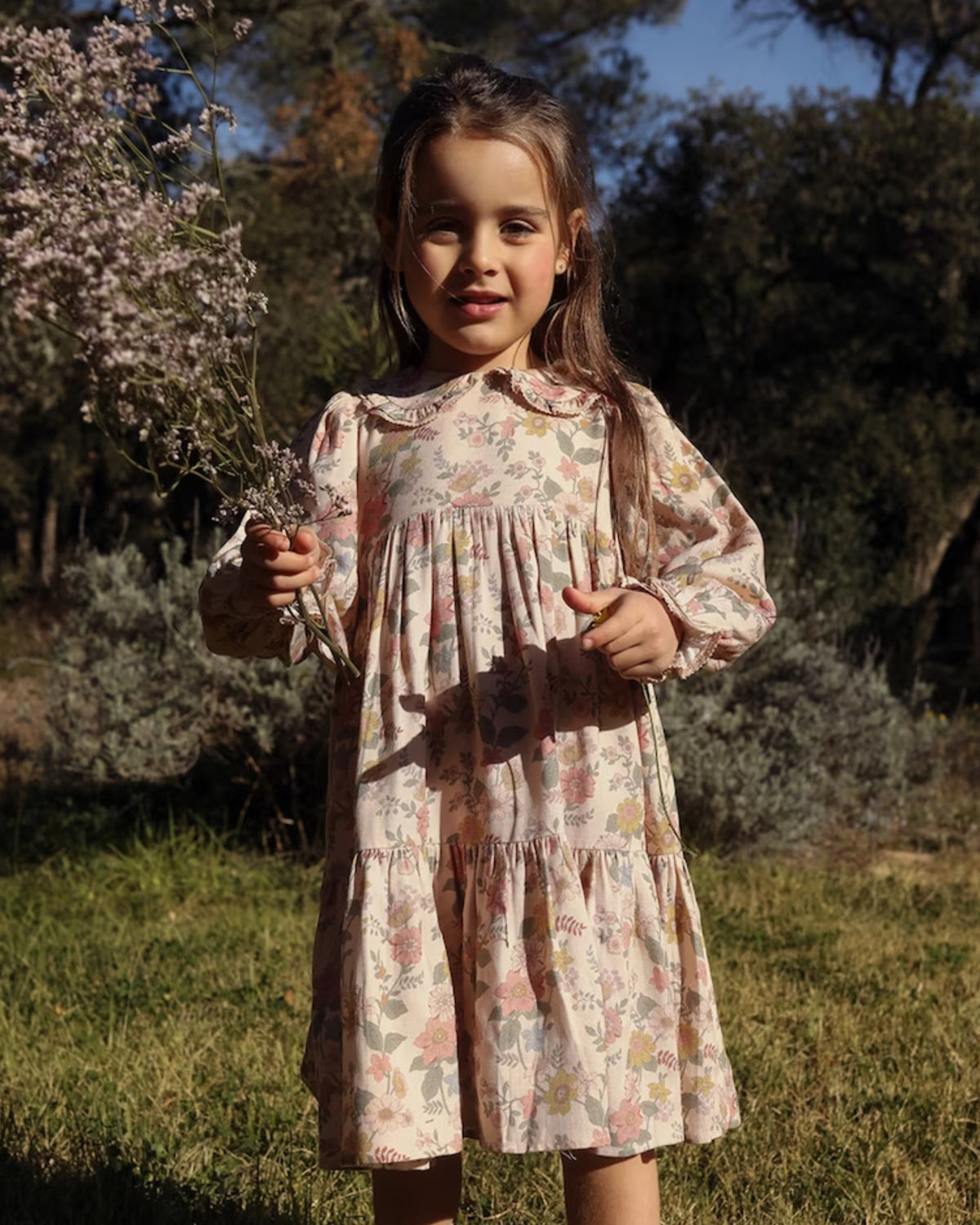 Early Sunday, Marguerite Dress in Bloom, made from Printed Viscose Twill fabric, featuring floral embroidery with frilled Peter Pan collar and gathered sleeves, shown in a front view of model wearing outdoors