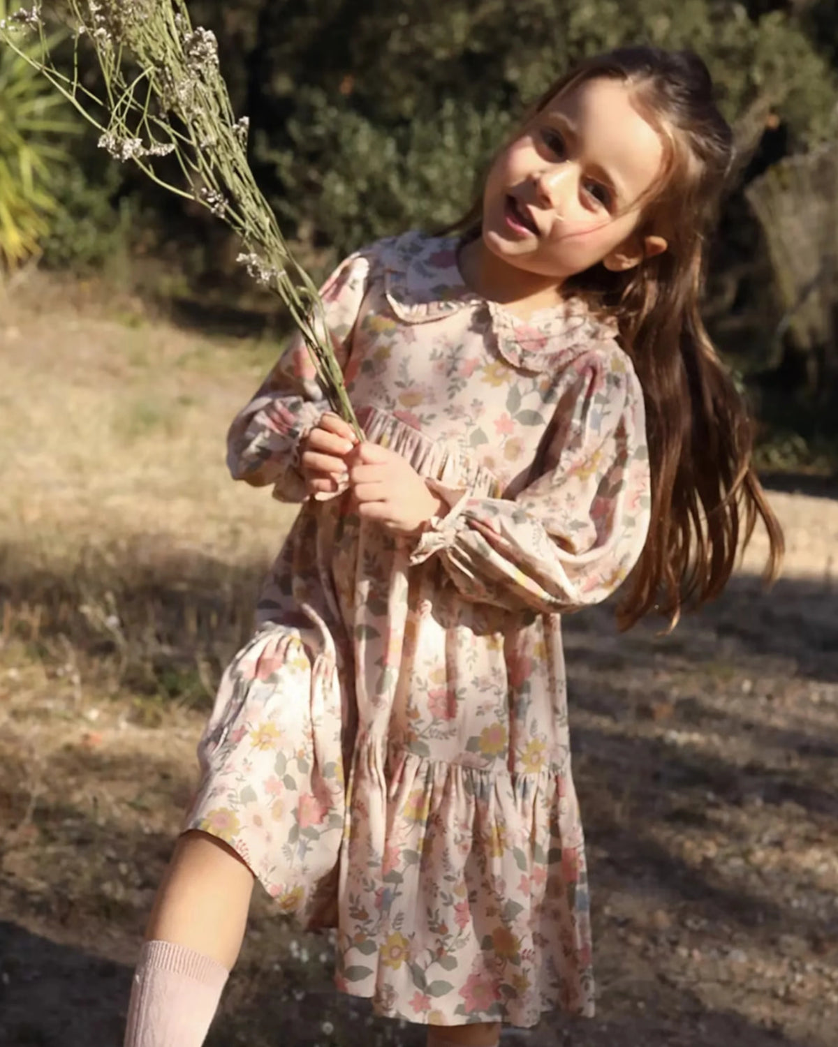 Early Sunday, Marguerite Dress in Bloom, made from Printed Viscose Twill fabric, featuring floral embroidery with frilled Peter Pan collar and gathered sleeves, shown in an angled view of a model wearing outdoors