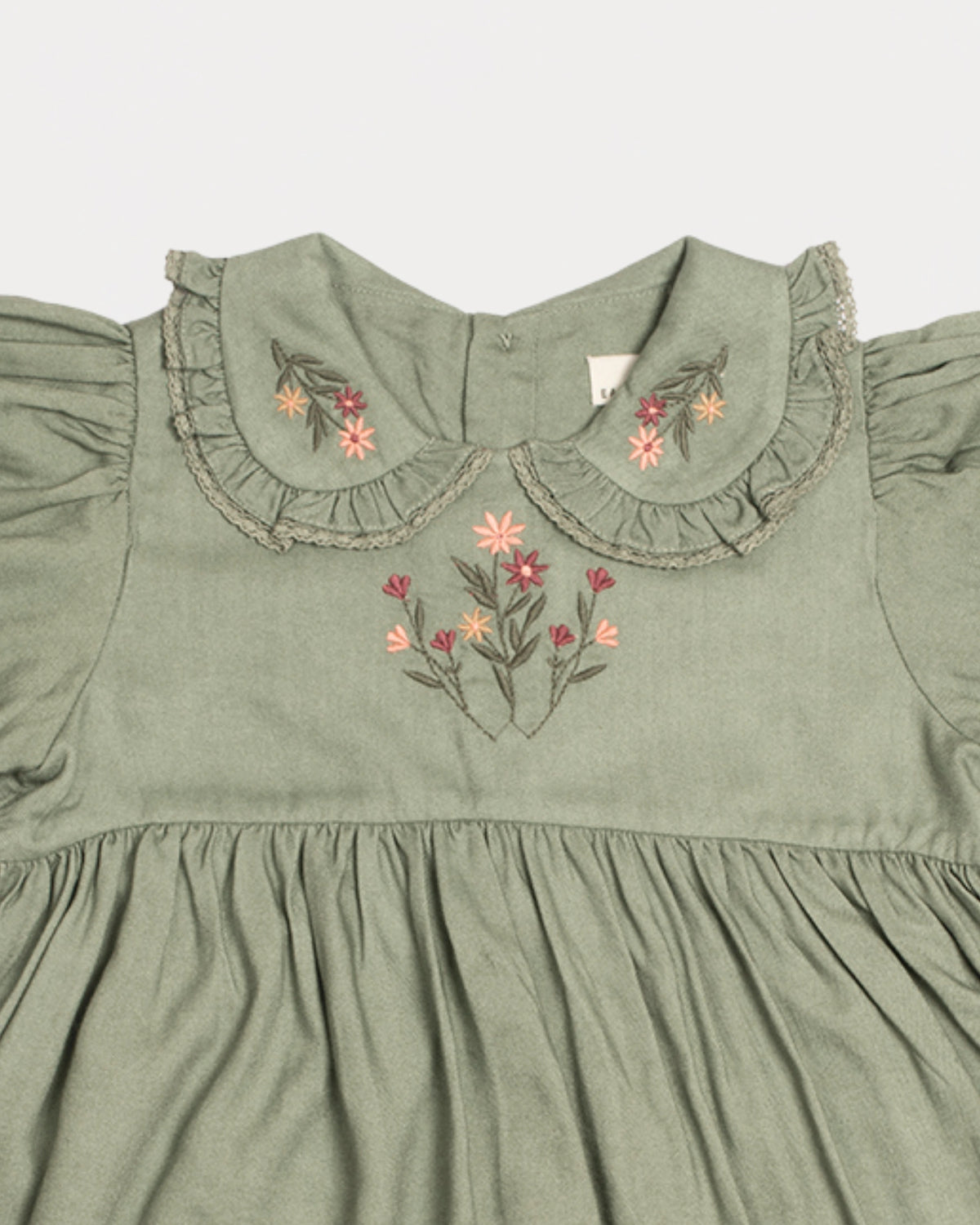 Early Sunday, Marguerite Dress in Sage Green, made from Viscose Drapey Twill fabric, featuring floral embroidery with frilled Peter Pan collar and gathered sleeves, shown in a closeup flat-lay view