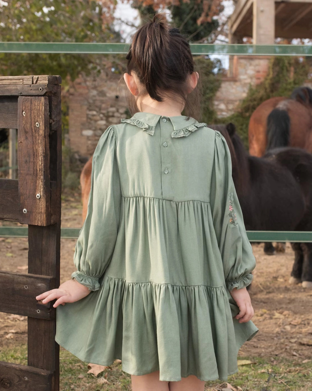 Early Sunday, Marguerite Dress in Sage Green, made from Viscose Drapey Twill fabric, featuring floral embroidery with frilled Peter Pan collar and gathered sleeves, shown in a back view of model wearing outdoors