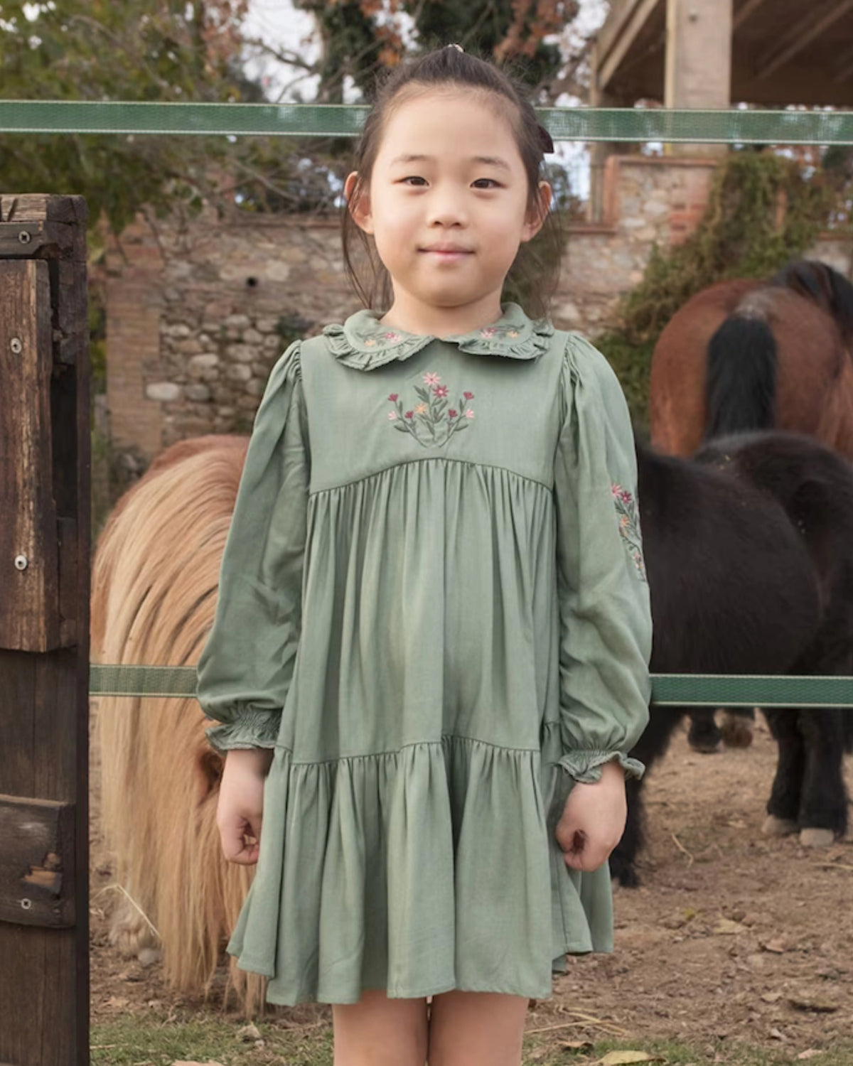 Early Sunday, Marguerite Dress in Sage Green, made from Viscose Drapey Twill fabric, featuring floral embroidery with frilled Peter Pan collar and gathered sleeves, shown in a front view of model wearing outdoors