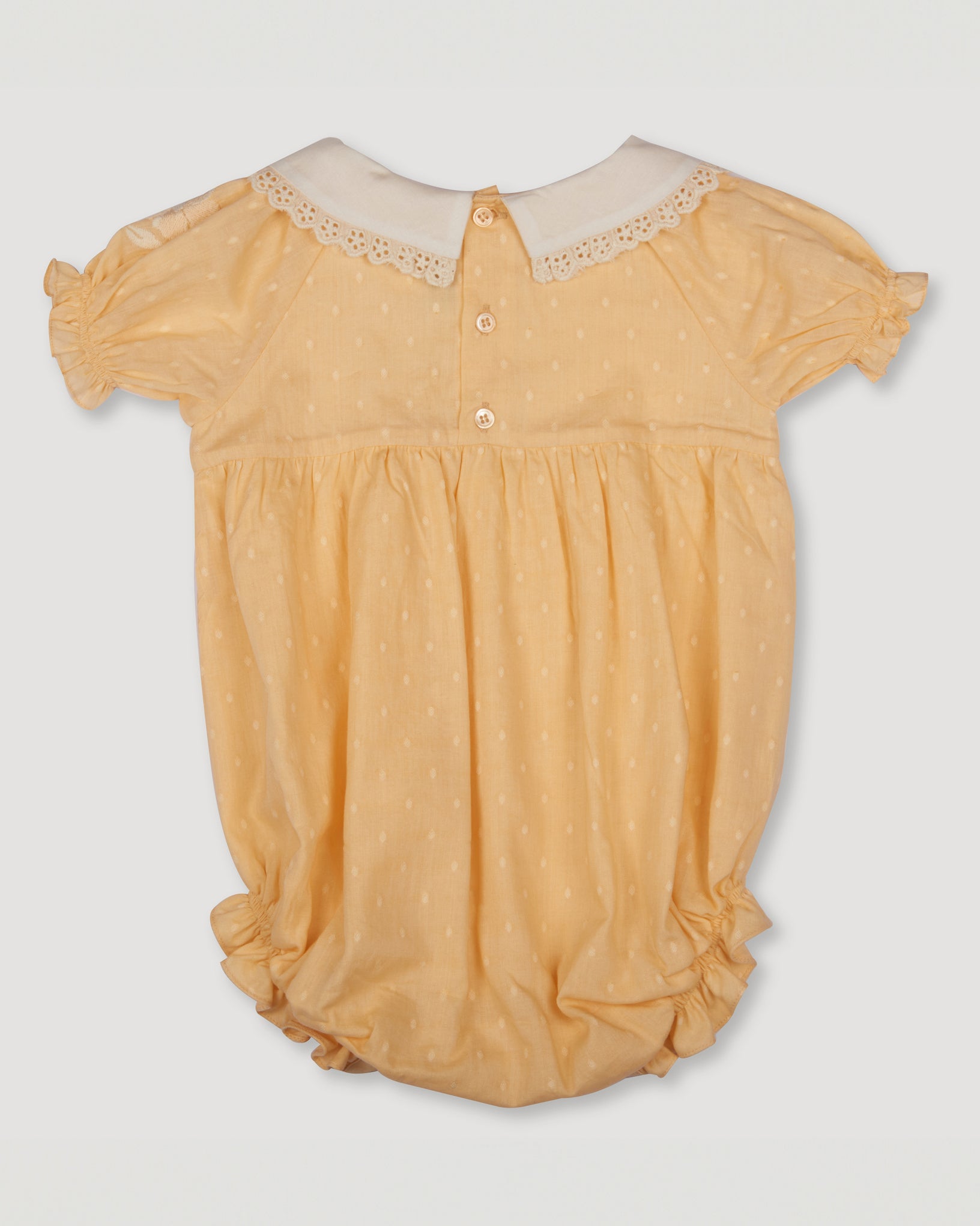 Early Sunday, Matilda Baby Bubble Romper in Vanilla color, made from Cotton Dobby Swiss Dots fabric, featuring ruffled neckline for a delicate touch and elasticated leg openings for a comfortable fit, shown in a back flat-lay view
