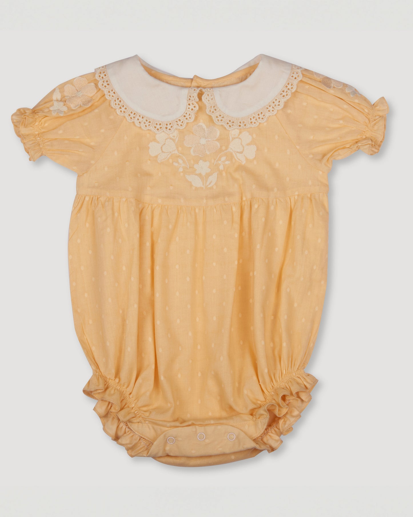 Early Sunday, Matilda Baby Bubble Romper in Vanilla color, made from Cotton Dobby Swiss Dots fabric, featuring ruffled neckline for a delicate touch and elasticated leg openings for a comfortable fit, shown in a front flat-lay view