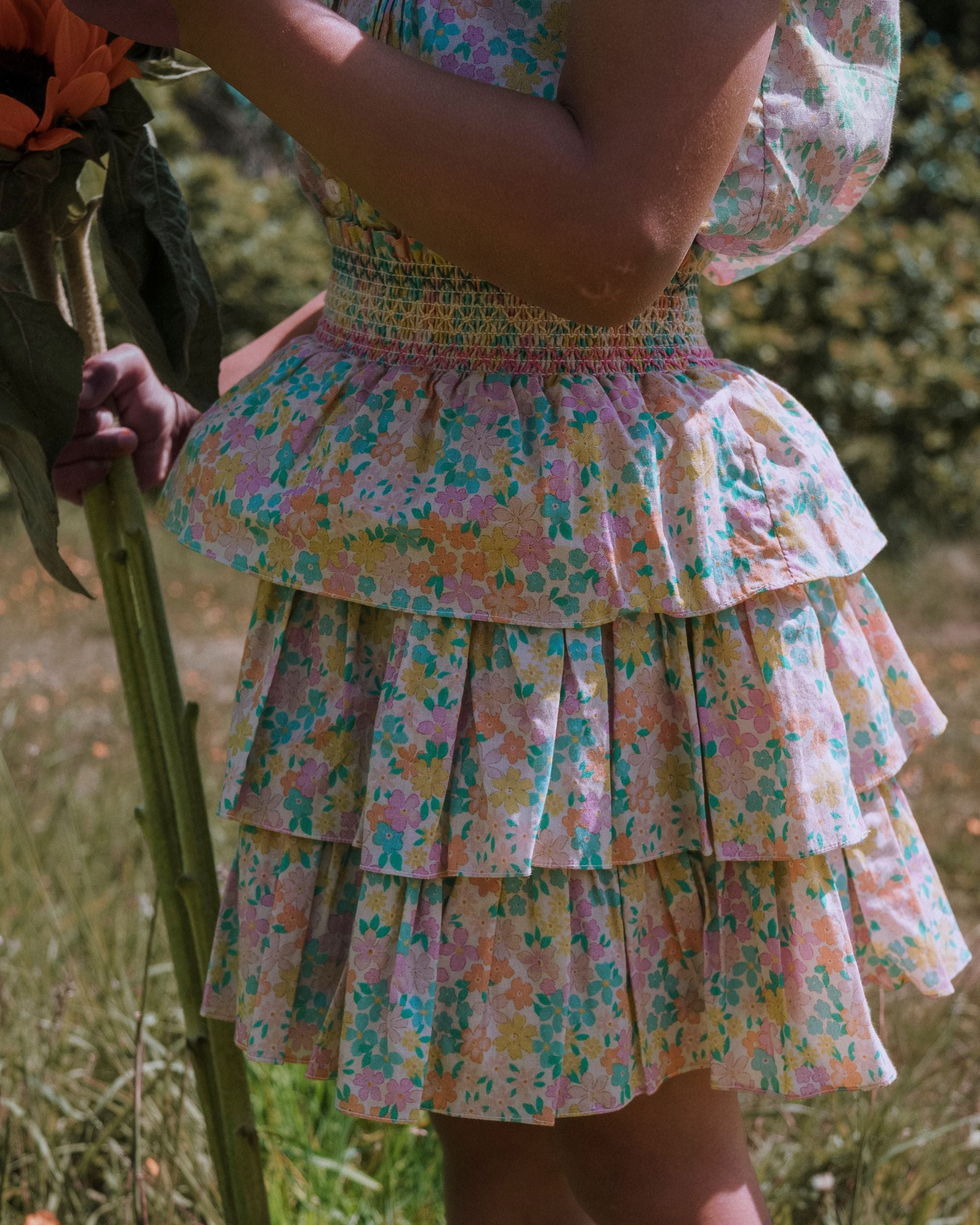 Early Sunday, Melissa Skirt in Emma Floral Mint color, made from Organic Printed Cotton Cambric fabric, featuring tiered frilly skirt with smocked waistband, shown in a close up shot of model wearing outdoors