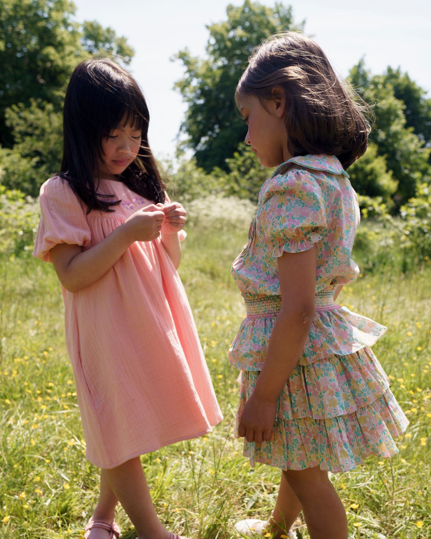 Early Sunday, Melissa Skirt in Emma Floral Mint color, made from Organic Printed Cotton Cambric fabric, featuring tiered frilly skirt with smocked waistband, shown in a side view of models playing outdoors
