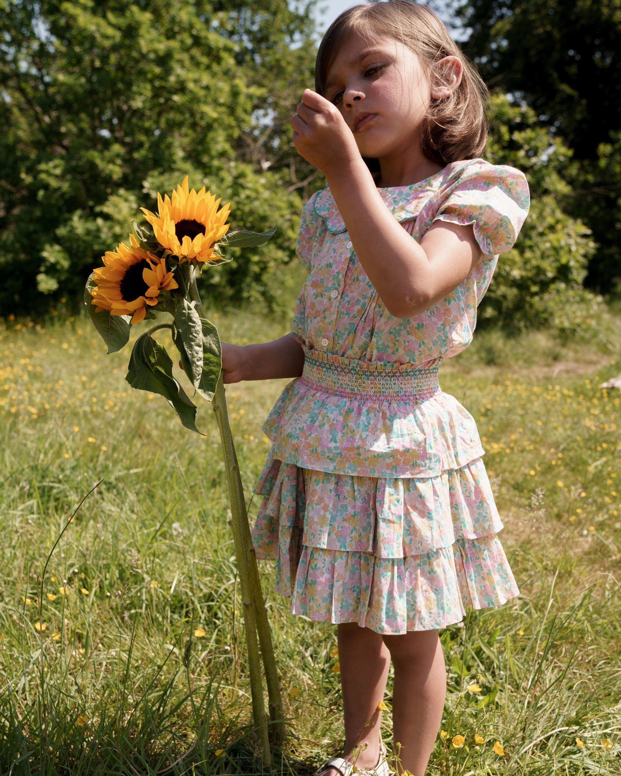 Early Sunday, Melissa Skirt in Emma Floral Mint color, made from Organic Printed Cotton Cambric fabric, featuring tiered frilly skirt with smocked waistband, shown in a side view of model playing outdoors