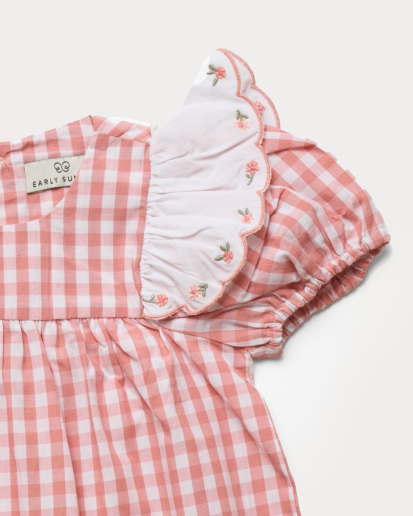 Early Sunday, Mia Baby Romper in Peony color, made from 100% Cotton Gingham Check fabric, featuring ruffled sleeves with rose embroidery, shown in a closeup flat-lay view