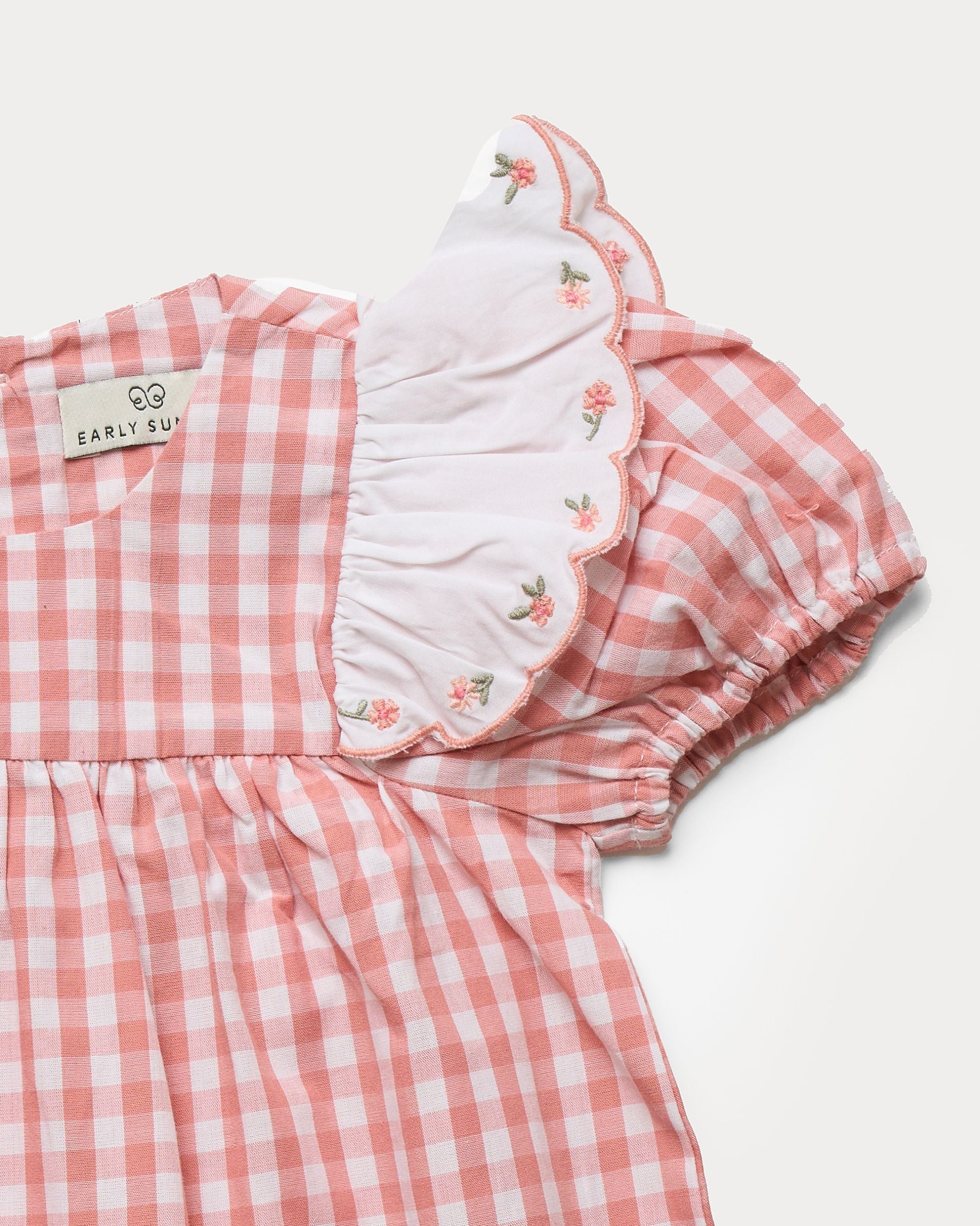 Early Sunday, Mia Baby Romper in Peony color, made from 100% Cotton Gingham Check fabric, featuring ruffled sleeves with rose embroidery, shown in a closeup flat-lay view