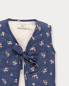 Early Sunday, Milly Baby Quilted Gilet in Ditsy Bouquet Navy, made from Printed Cotton Satin fabric, featuring a sleeveless jacket with a bow tie, shown in a closeup flat-lay view