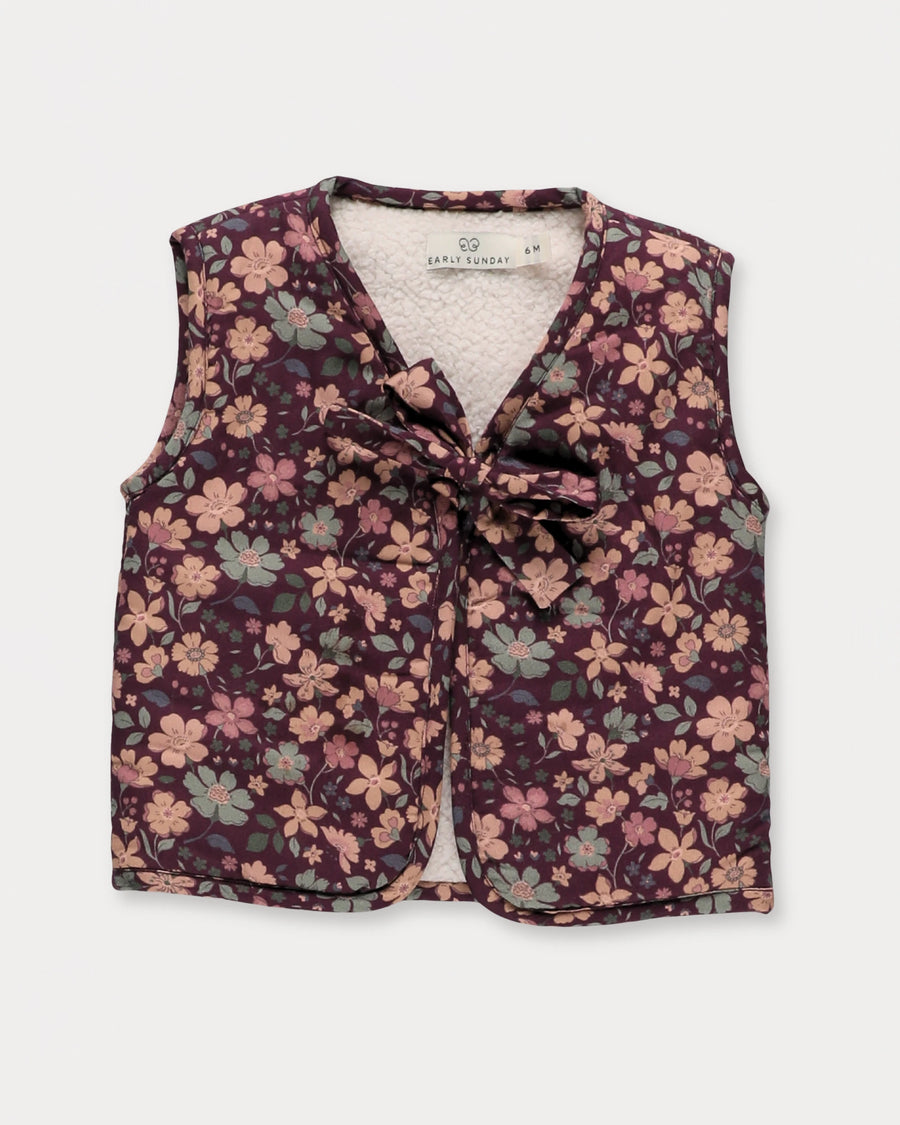 Early Sunday, Milly Baby Quilted Gilet in Garden Flowers Plum, made from Printed Cotton Satin fabric, featuring a sleeveless jacket with a bow tie, shown in a front flat-lay view
