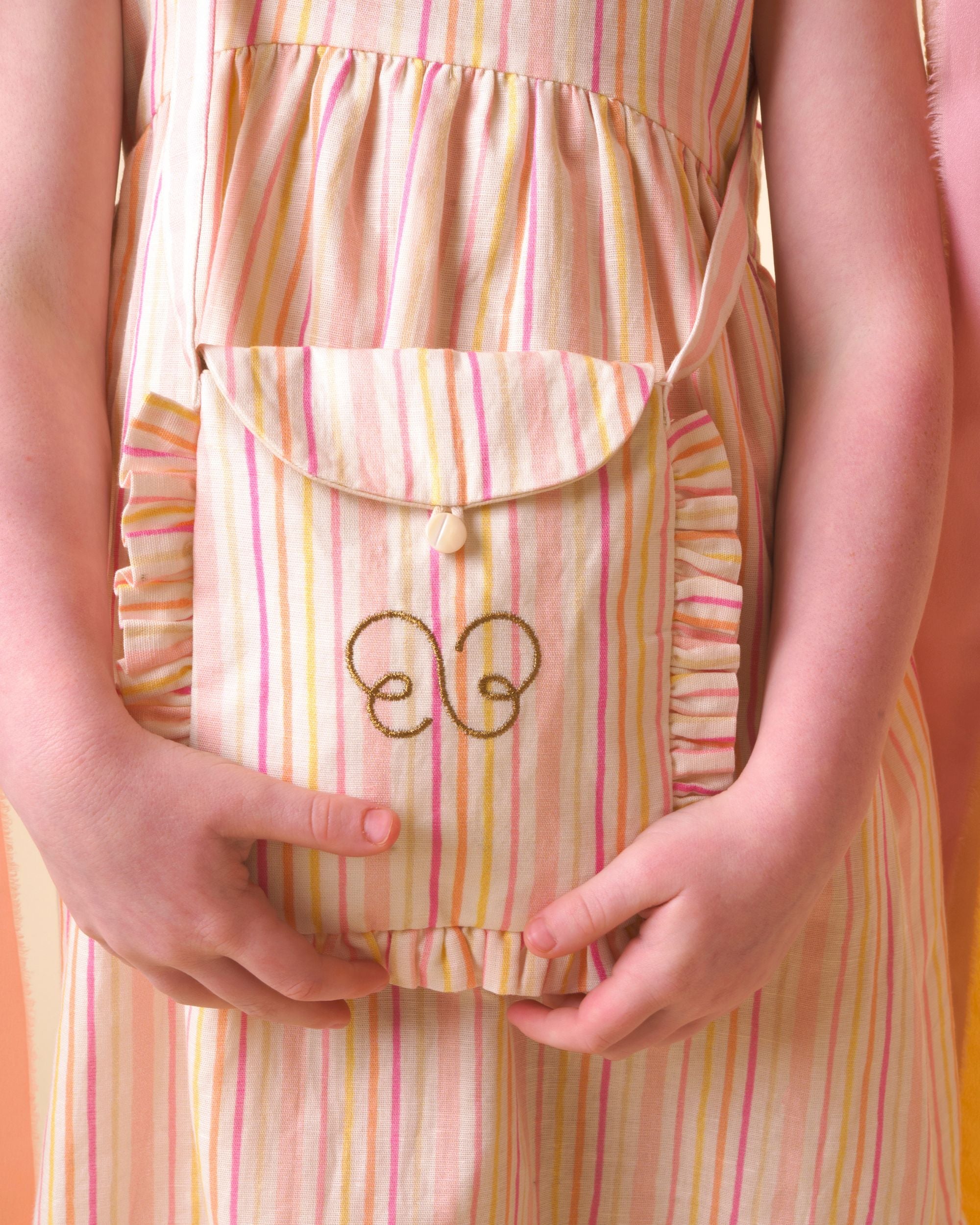 Early Sunday, Miss Sunday Sling in Pink Stripes print, made from 70% Cotton, 30% Linen fabric, featuring a frill detailed sling purse with flap closure, shown in a close up shot of model wearing it