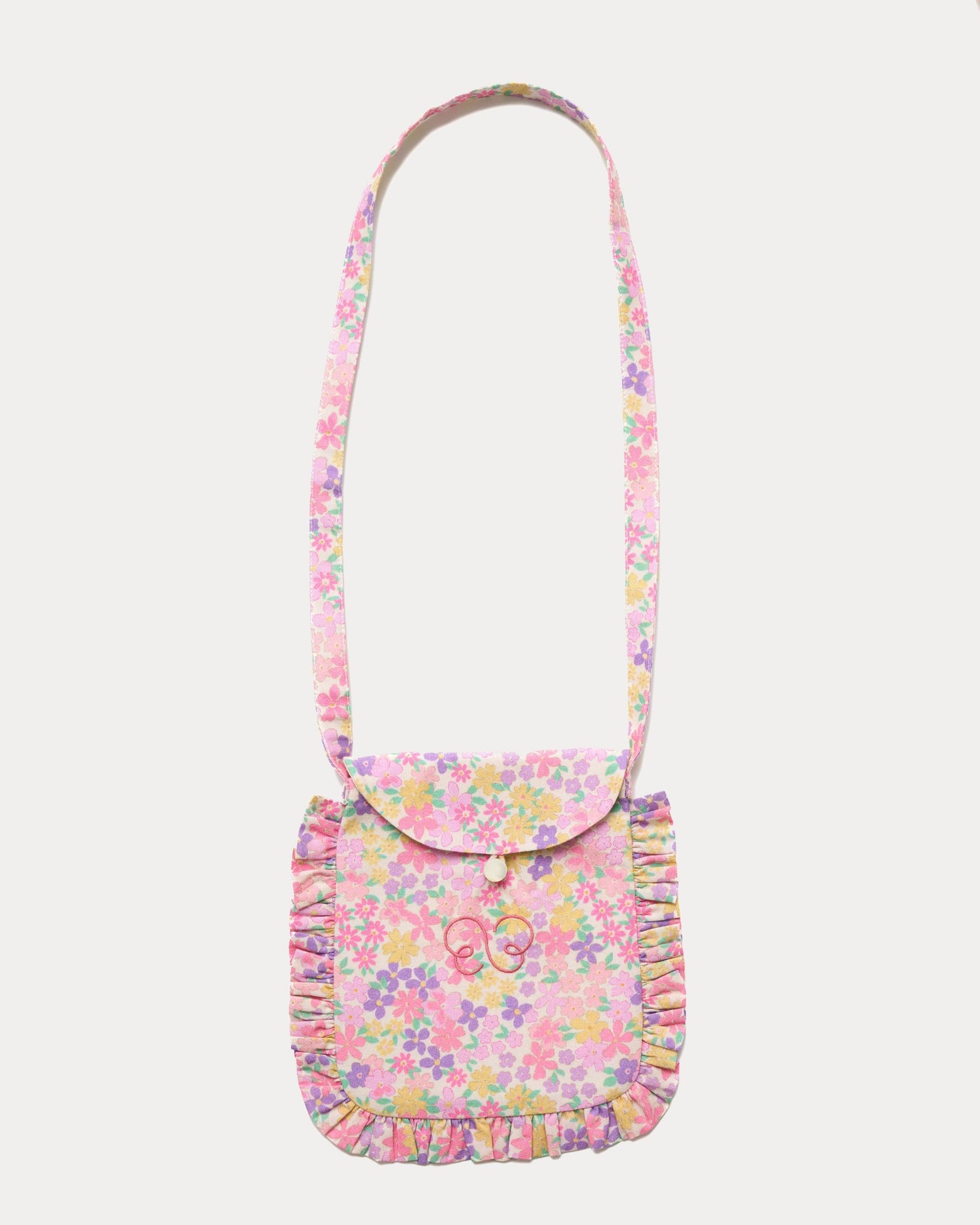 Early Sunday, Miss Sunday Sling in Emma Floral Purple color, made from Organic Printed Cotton Cambric fabric, featuring a frill detailed sling purse with flap closure, shown in front flat-lay view