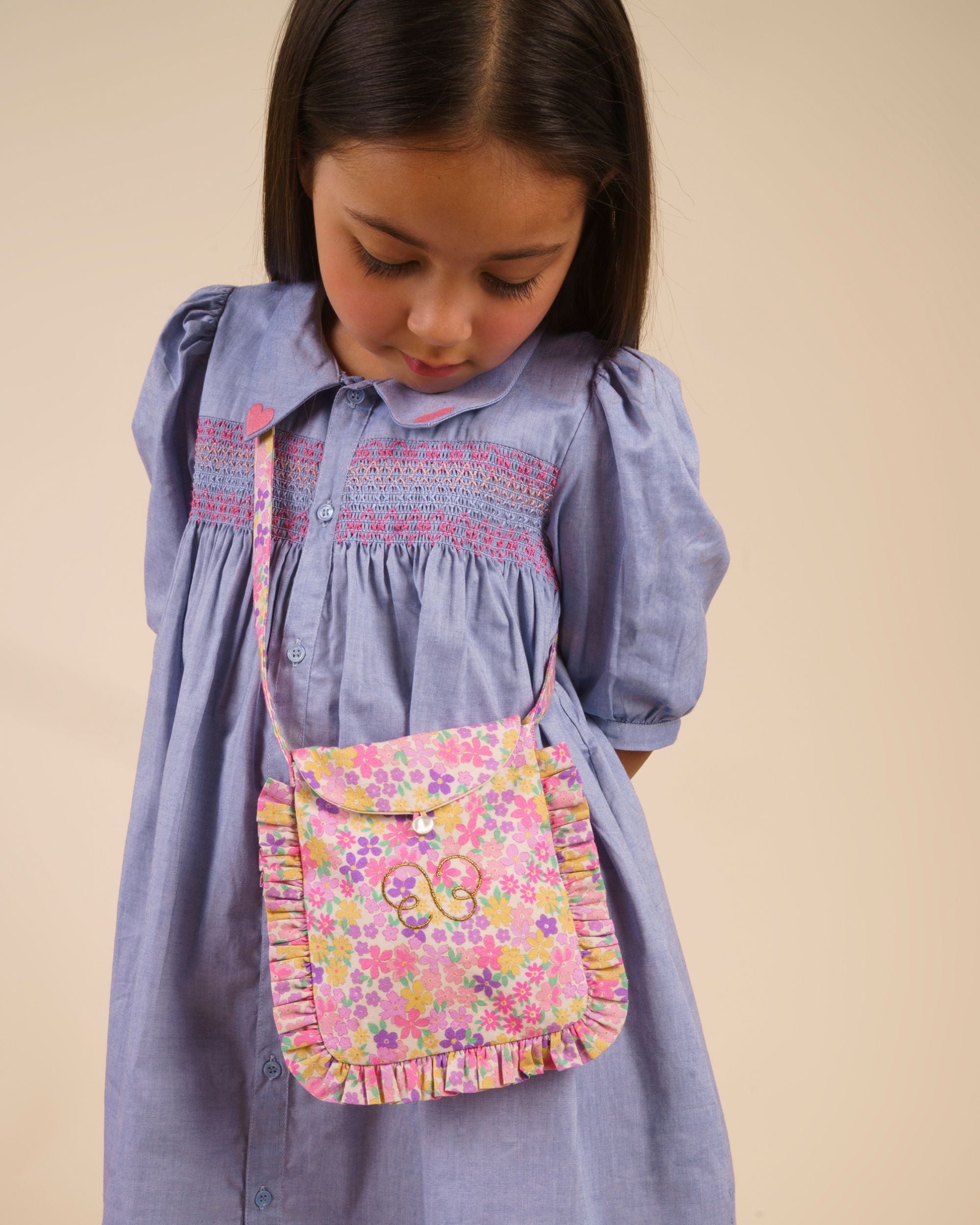 Early Sunday, Miss Sunday Sling in Emma Floral Purple color, made from Organic Printed Cotton Cambric fabric, featuring a frill detailed sling purse with flap closure, shown in front view of model wearing it