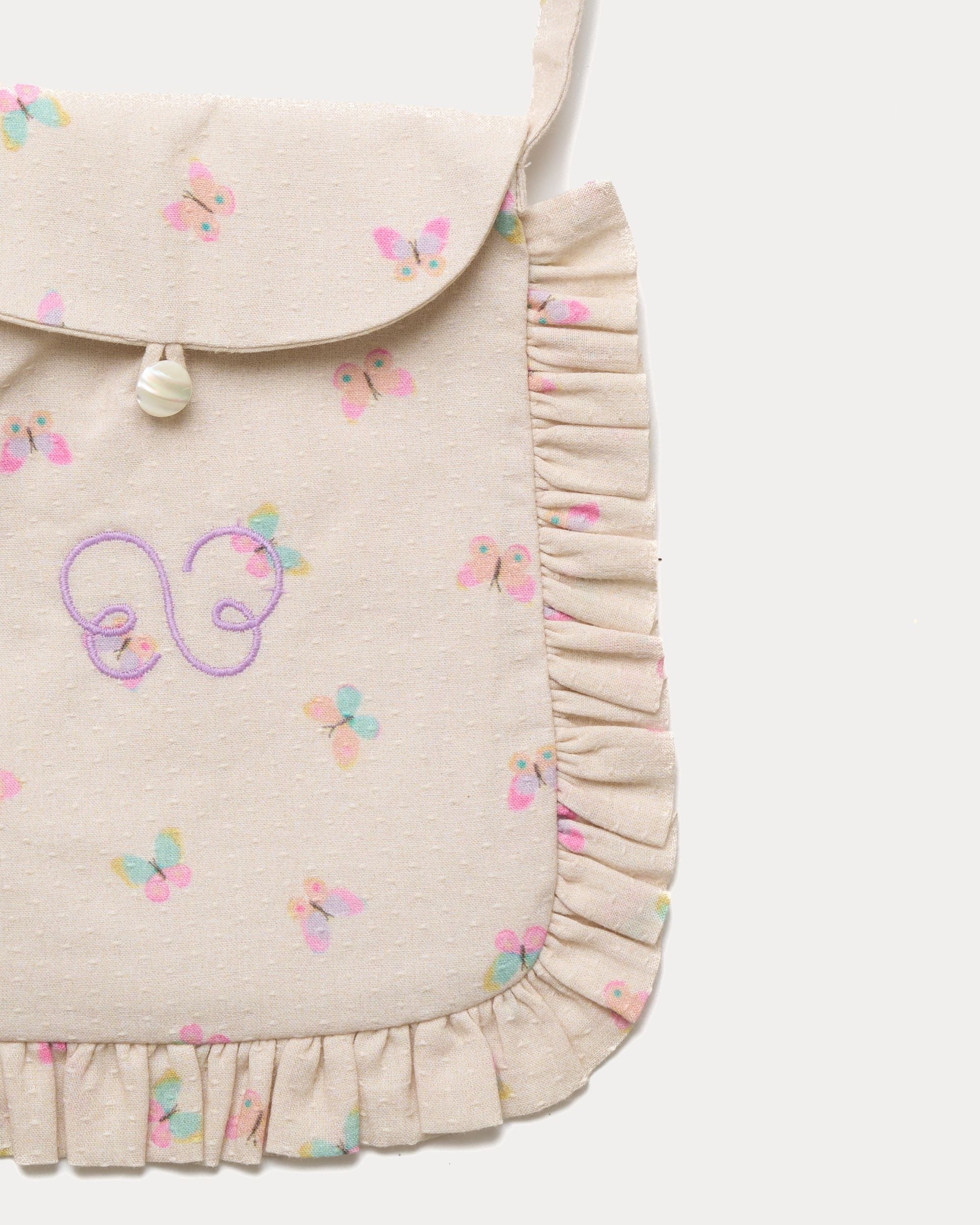Early Sunday, Miss Sunday Sling in Butterflies print, made from Printed Cotton Tiny Swiss Dobby fabric, featuring a frill detailed sling purse with flap closure, shown in a closeup flat-lay view
