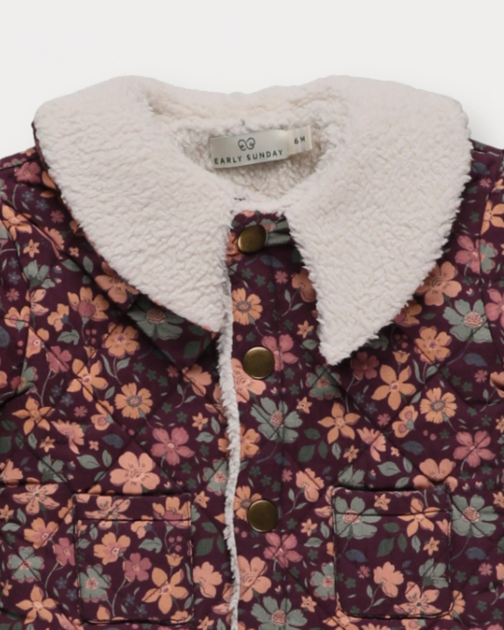 Early Sunday, Molly Baby Quilted Jacket in Garden Flowers Plum, made from Printed Cotton Satin fabric, featuring a sherpa collar & cuffed sleeves with snap button closure, shown in a closeup flat-lay view
