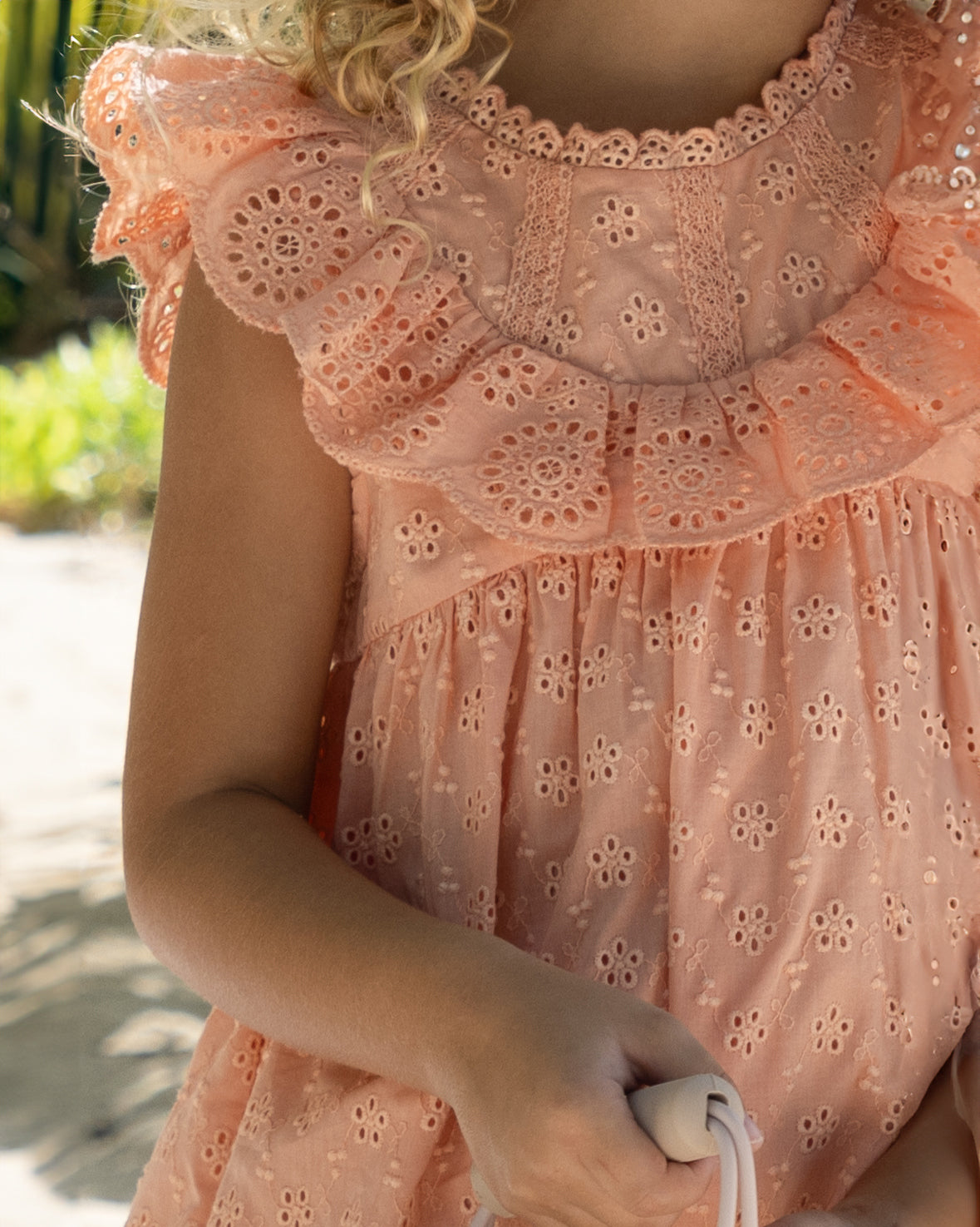 Early Sunday, Natasha Dress in Strawberry color, made from All-Over Eyelet Embroidered Cotton Schifflie fabric, featuring flattering fit with delicate finishes, combining style and functionality for an effortlessly elegant look, shown in a close up shot of model wearing outdoors