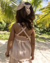 Early Sunday, Olivia Blouse in Pink Sand color, made from Canvas 70% Cotton 30% Linen fabric, featuring smocked bodice for a flexible fit, cross-back strap sand a flared hem, shown in a back view of model wearing it