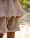 Early Sunday, Olivia Blouse in Pink Sand color, made from Canvas 70% Cotton 30% Linen fabric, featuring smocked bodice for a flexible fit, cross-back strap sand a flared hem, shown in a detailed print view of model wearing it