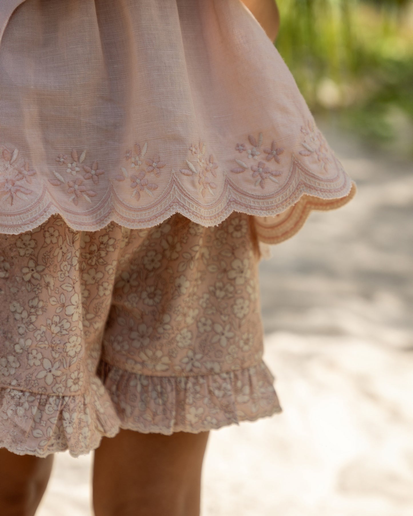 Early Sunday, Olivia Blouse in Pink Sand color, made from Canvas 70% Cotton 30% Linen fabric, featuring smocked bodice for a flexible fit, cross-back strap sand a flared hem, shown in a detailed print view of model wearing it
