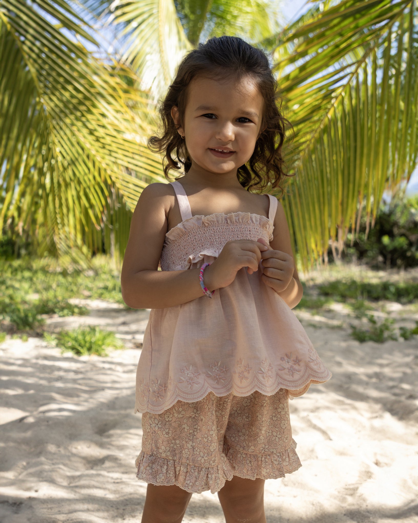 Early Sunday, Olivia Blouse in Pink Sand color, made from Canvas 70% Cotton 30% Linen fabric, featuring smocked bodice for a flexible fit, cross-back strap sand a flared hem, shown in a front view of model wearing it