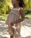 Early Sunday, Olivia Blouse in Pink Sand color, made from Canvas 70% Cotton 30% Linen fabric, featuring smocked bodice for a flexible fit, cross-back strap sand a flared hem, shown in a side view of model wearing it