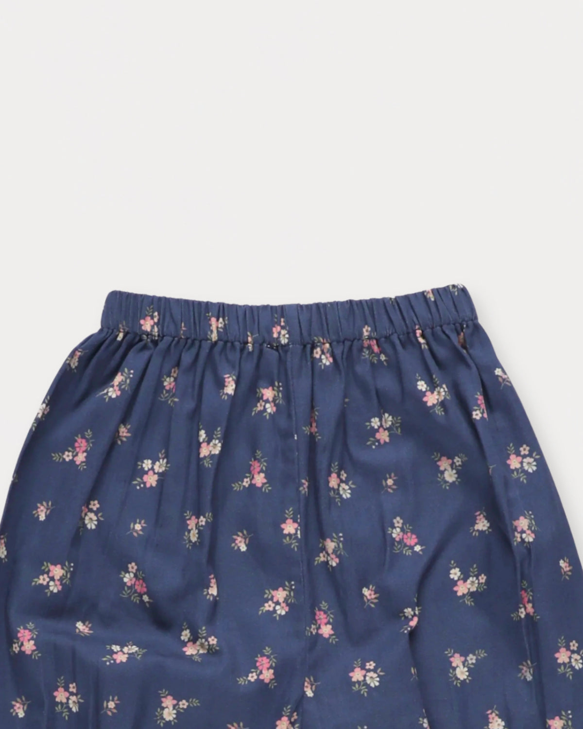 Early Sunday, Poppy Baby Bloomer Trousers in Ditsy Bouquet Navy, made from Printed Cotton Satin fabric, featuring an elasticated waistband & ruffled cuffs at the ankles, shown in a closeup flat-lay view