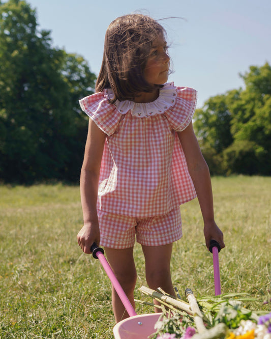 Early Sunday, Roman Cotton Gingham Check Short in Peony color, made from 100% Cotton fabric, featuring a relaxed silhouette with a comfortable elastic waistband, shown in a front view of model wearing outdoors