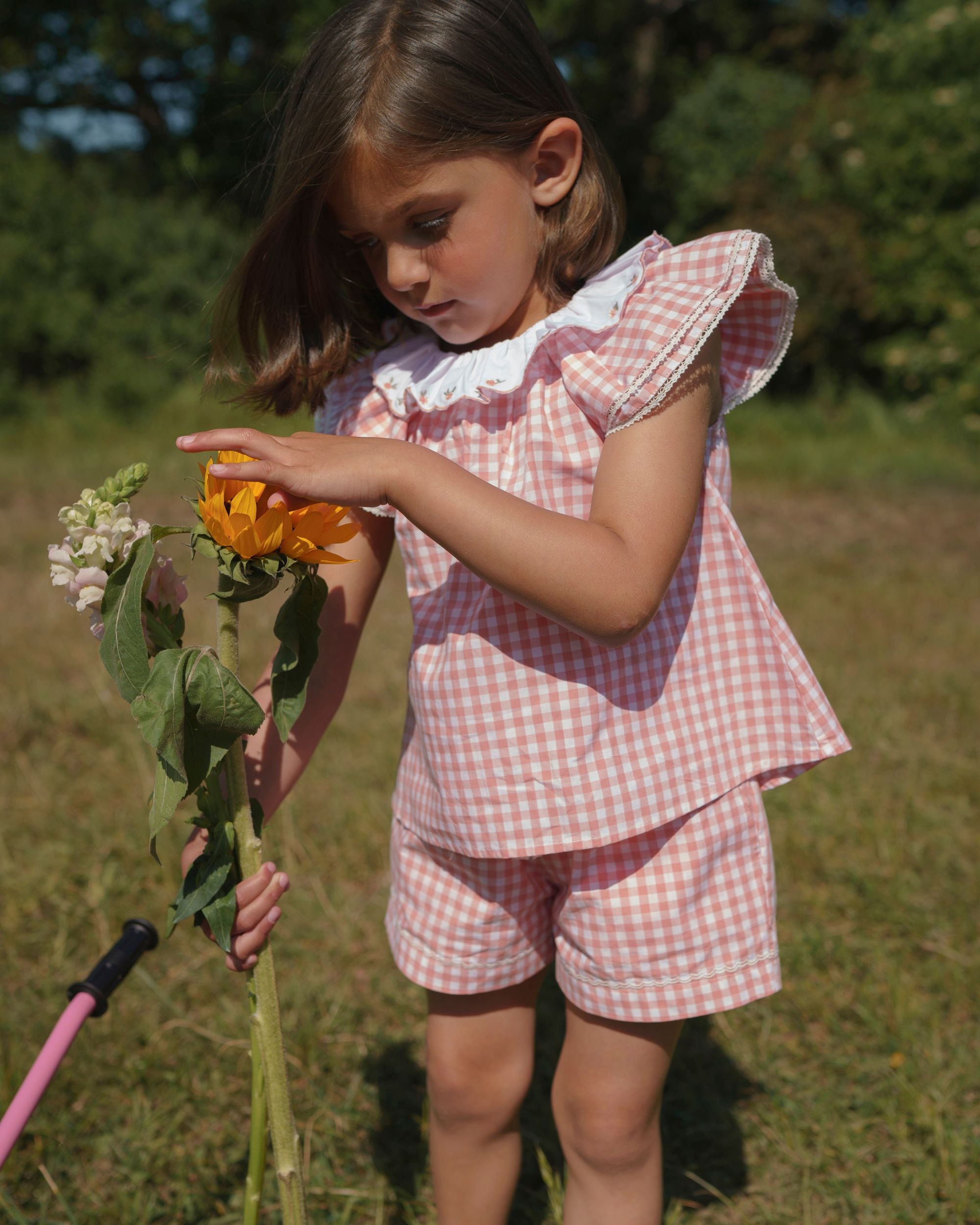 Early Sunday, Roman Cotton Gingham Check Short in Peony color, made from 100% Cotton fabric, featuring a relaxed silhouette with a comfortable elastic waistband, shown in a side view of model playing outdoors