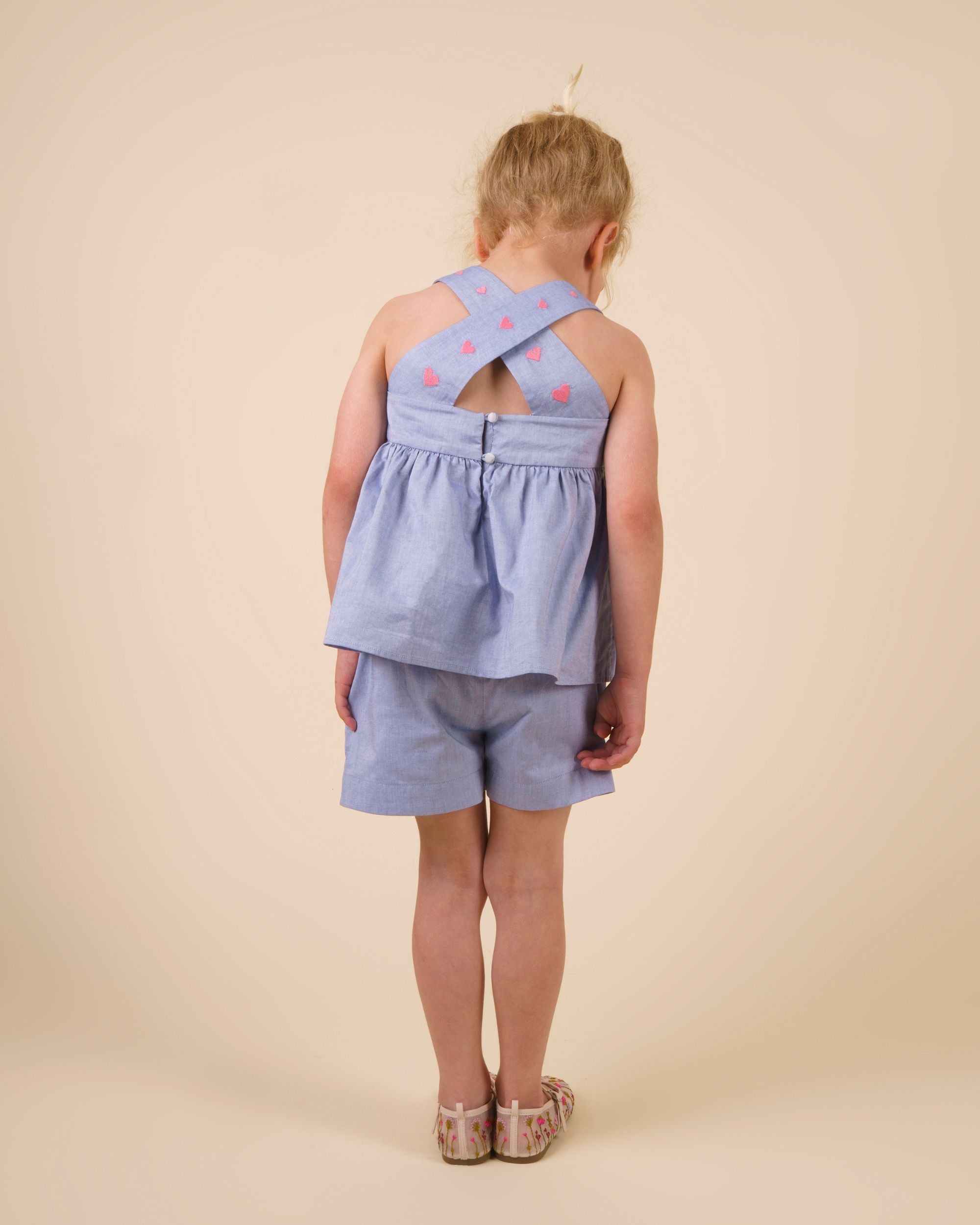 Early Sunday, Roman Short in Summer Sky color, made from 100% Cotton Chambray fabric, featuring a relaxed fit with an elastic waistband & beautiful embroidery, shown in a back view of a model wearing it in a studio setting