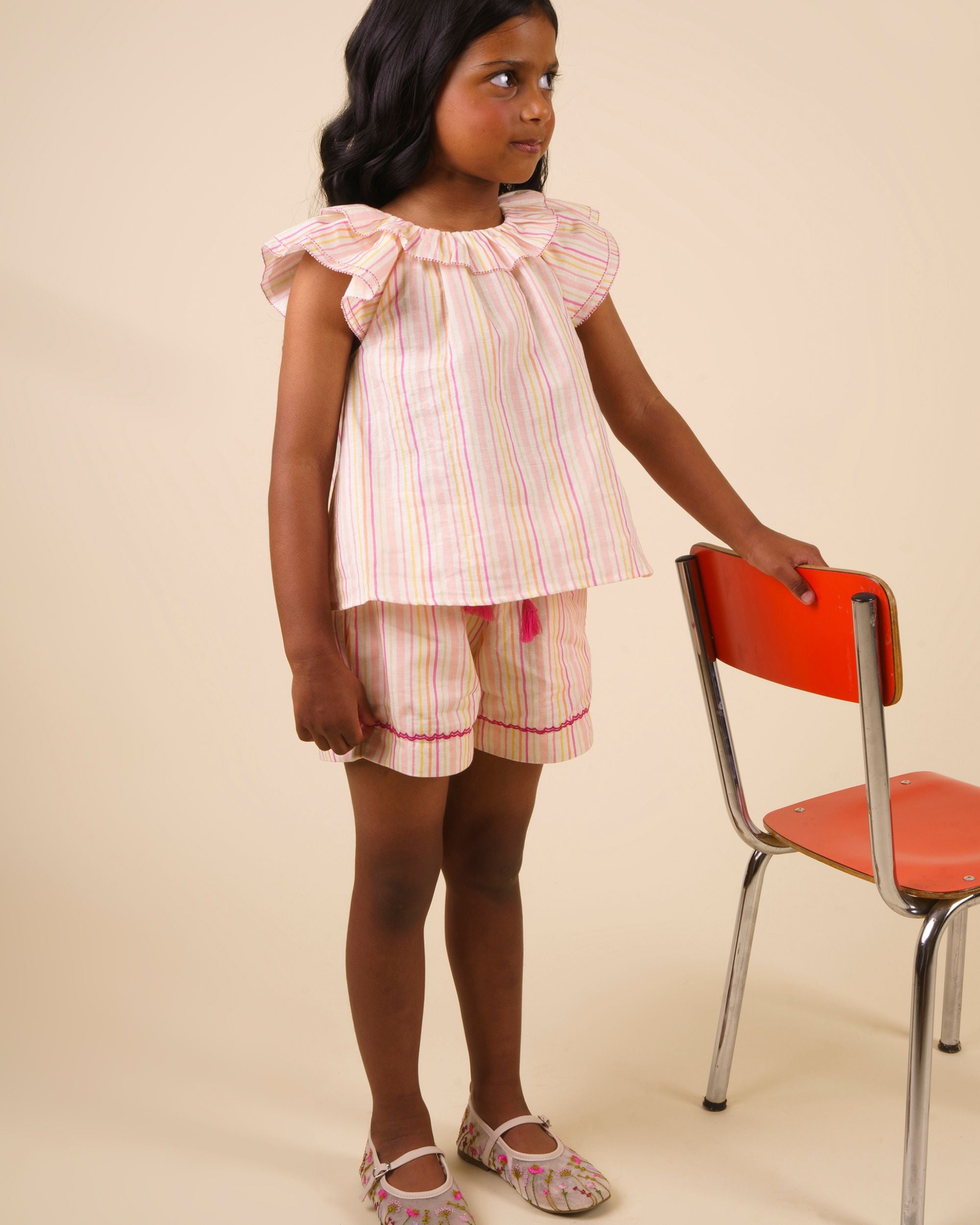 Early Sunday, Roman Short in Pink Strips print, made from 70% Cotton 30% Linen fabric, featuring a relaxed fit with an elastic waistband & striped design, shown in an angled view of a model wearing it in a studio setting