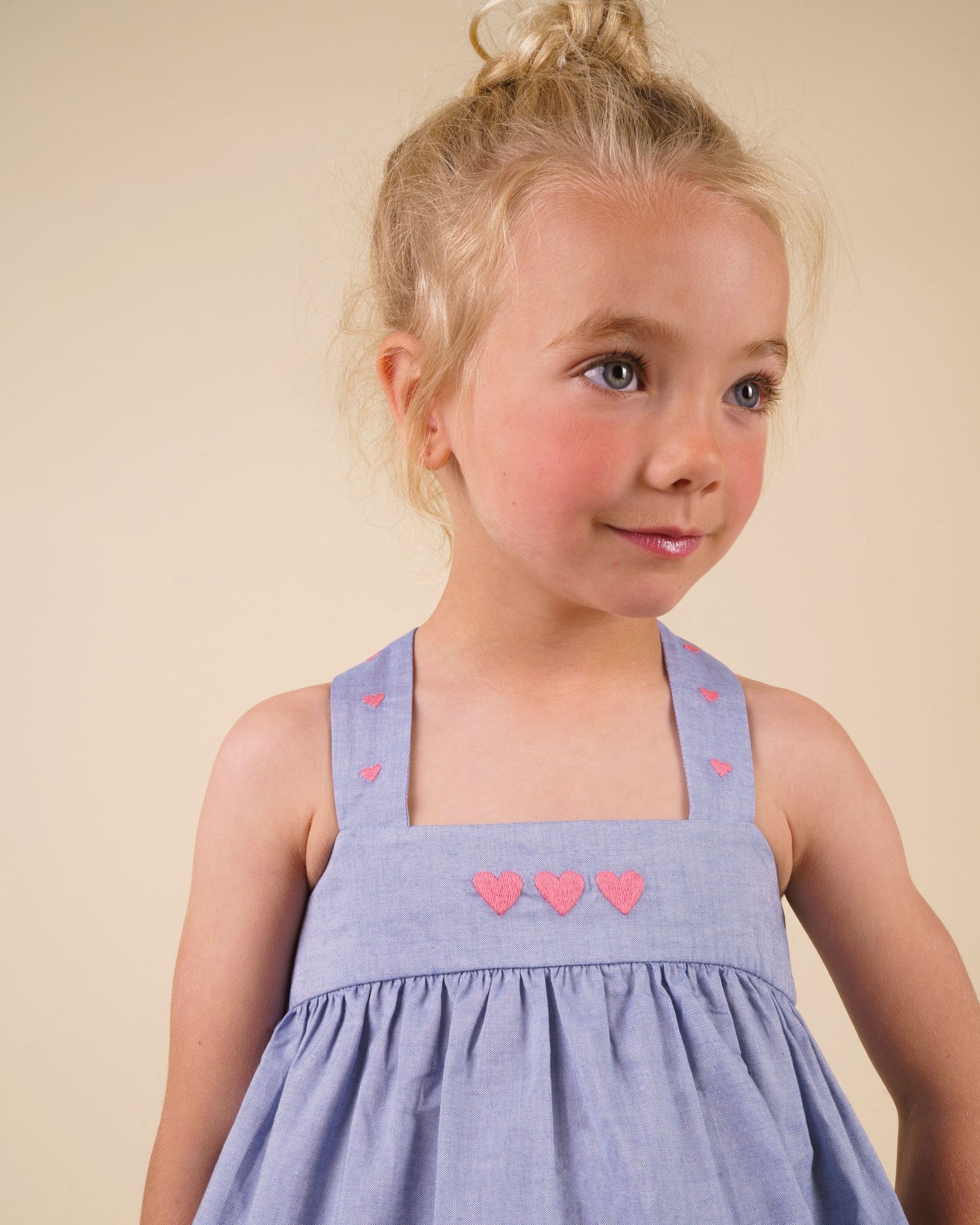 Early Sunday, Romy Blouse in Summer Sky color, made from  100% Cotton Chambray fabric, featuring a sleeveless design with cross-back straps, a gathered waist & a beautiful embroidery, shown in a close-up shot of a model wearing it during a studio shoot