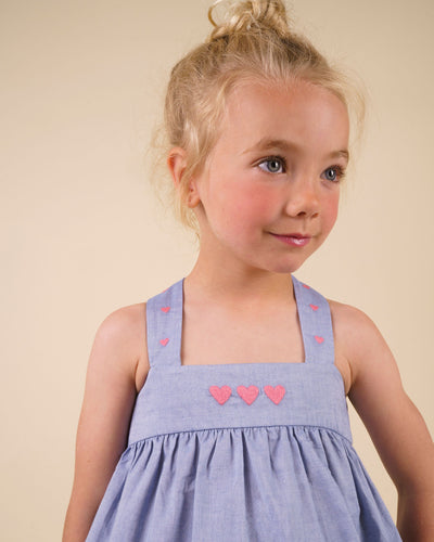 Early Sunday, Romy Blouse in Summer Sky color, made from  100% Cotton Chambray fabric, featuring a sleeveless design with cross-back straps, a gathered waist & a beautiful embroidery, shown in a close-up shot of a model wearing it during a studio shoot