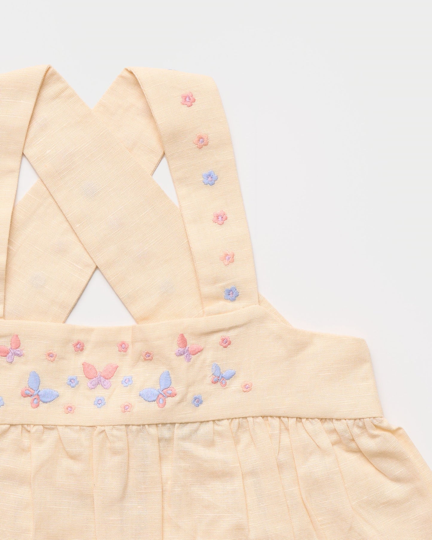 Early Sunday, Romy Blouse in Sand color, made from 70% Cotton 30% Linen fabric, featuring a sleeveless design with cross-back straps, a gathered waist & a beautiful embroidery, shown in a closeup flat-lay view