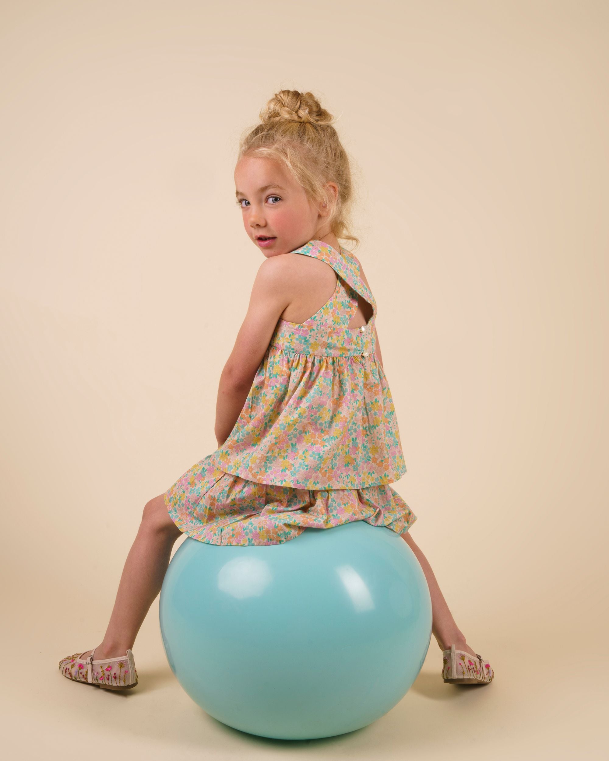 Early Sunday, Romy Blouse in Emma Floral Mint color, made from Organic Printed 60s Cotton Cambric fabric, featuring a sleeveless design with cross-back straps, a gathered waist & a soft flared silhouette, shown in a back view of a model wearing it in a studio setting