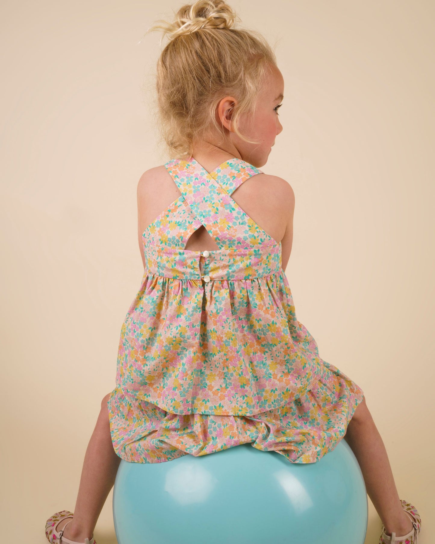 Early Sunday, Romy Blouse in Emma Floral Mint color, made from Organic Printed 60s Cotton Cambric fabric, featuring a sleeveless design with cross-back straps, a gathered waist & a soft flared silhouette, shown in a close-up back view of a model wearing it in a studio setting