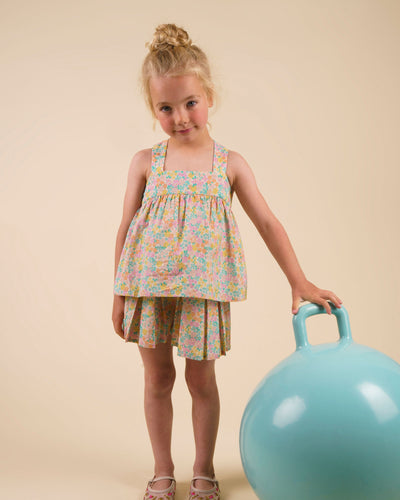 Early Sunday, Romy Blouse in Emma Floral Mint color, made from Organic Printed 60s Cotton Cambric fabric, featuring a sleeveless design with cross-back straps, a gathered waist & a soft flared silhouette, shown in a front view of a model wearing it in a studio setting