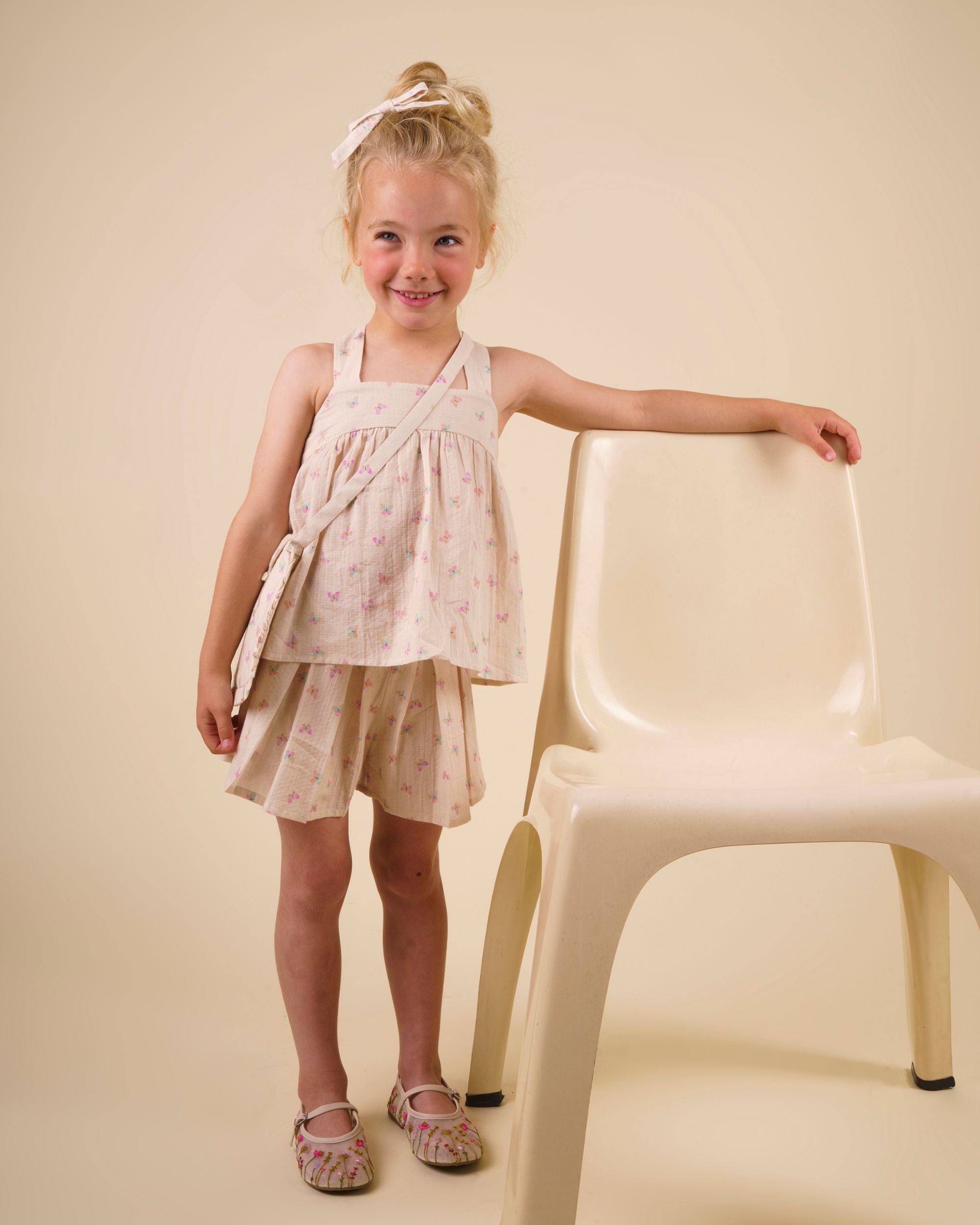 Early Sunday, Romy Blouse in Butterflies print, made from Printed Cotton Tiny Swiss Dobby fabric, featuring a sleeveless design with cross-back straps, a gathered waist & a soft flared silhouette, shown in front view of a model wearing it in a studio setting